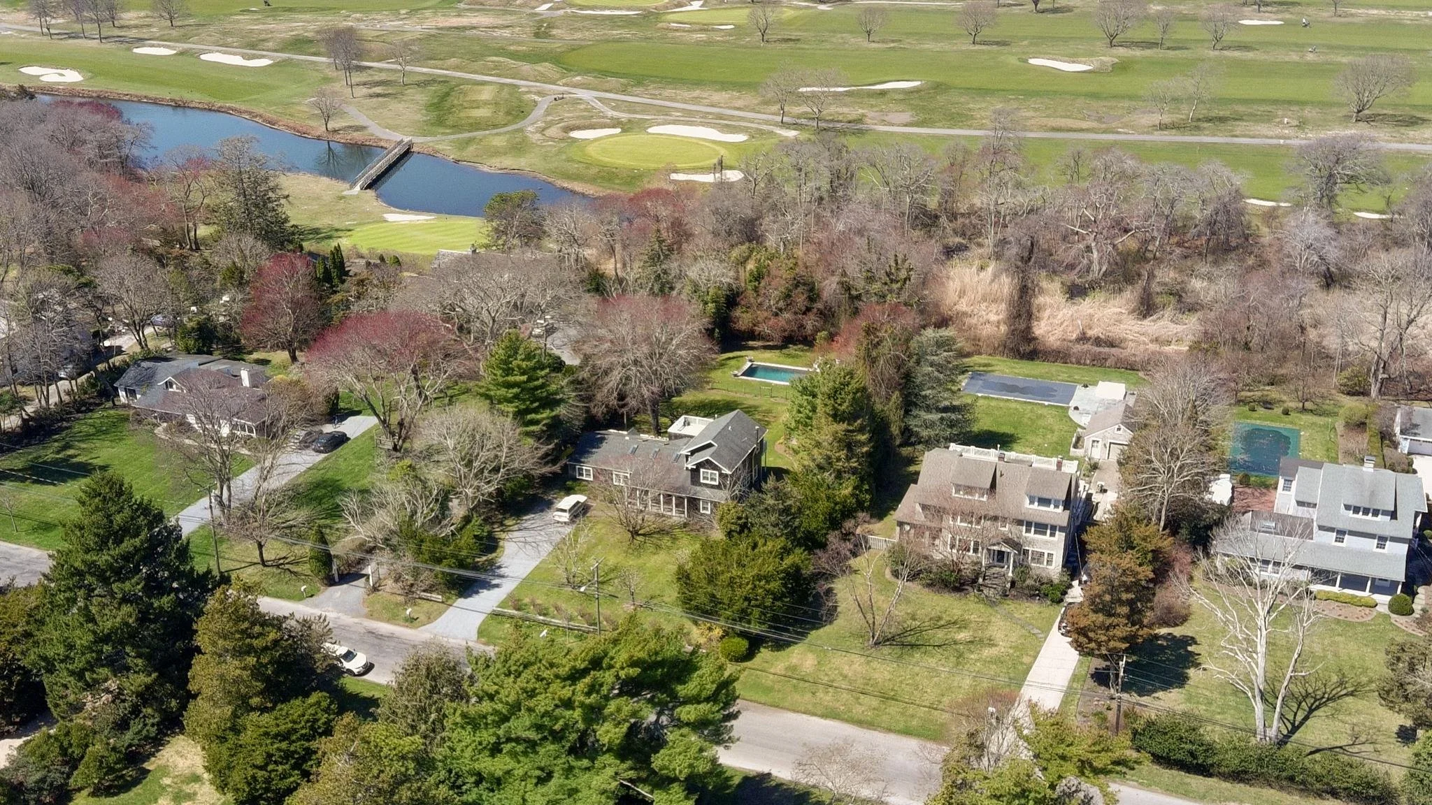 Aerial view of suburban neighborhood with houses, trees, a lake, golf course, and green spaces.