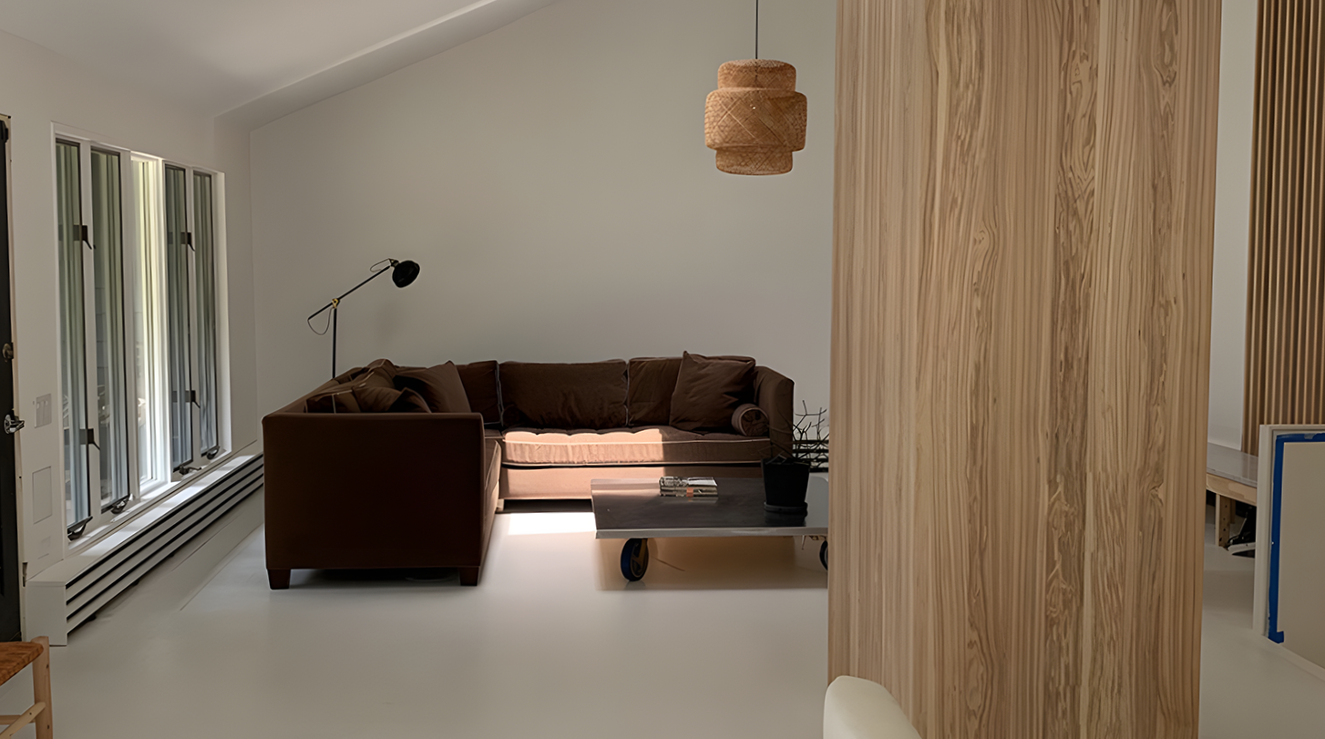 Living room with a brown sofa, a black floor lamp, a wooden coffee table on wheels, a black potted plant, and a light fixture hanging from the ceiling. There are windows with three vertical panes and white walls.