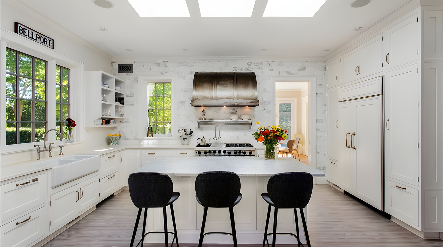 A bright, modern kitchen with white cabinetry, a large white island with black chairs, a stainless steel range hood, a stove, white marble backsplash, two windows, and a view into an adjacent dining area.