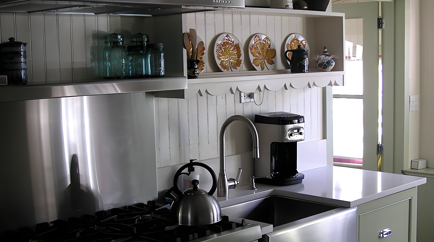 Kitchen with a stainless steel stove, kettle, sink, coffee machine, open shelf with plates and jars, and a window door.