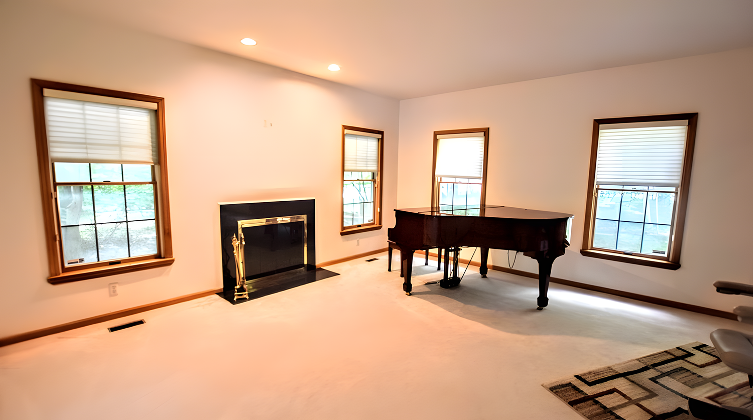 Living room with four windows, a black fireplace, a grand piano, and a rug in the corner.