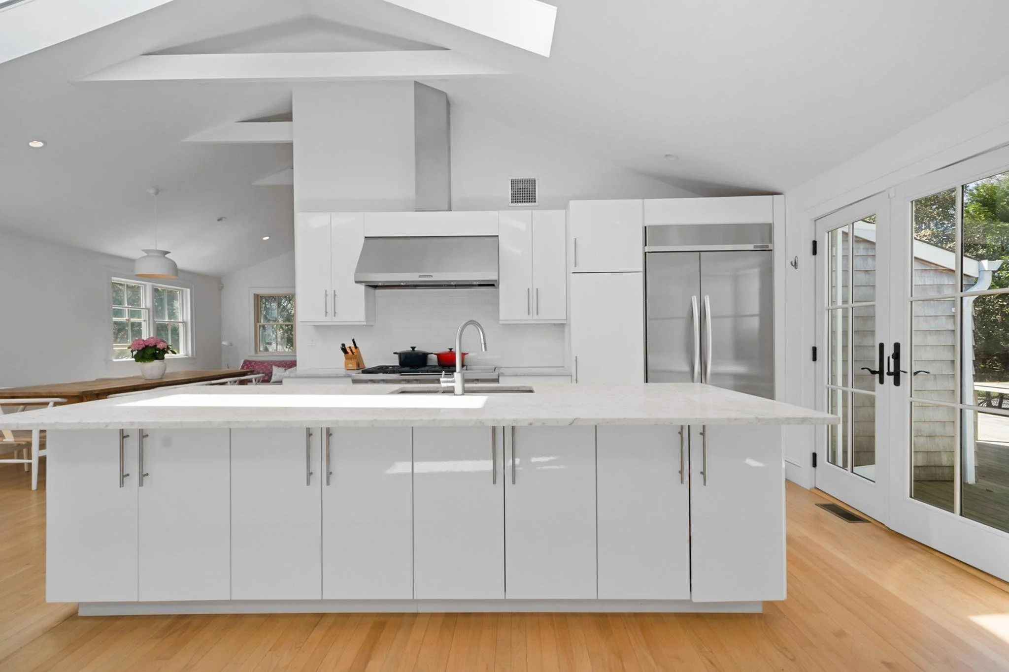 Modern white kitchen with center island, stainless steel appliances, and French doors leading outside.