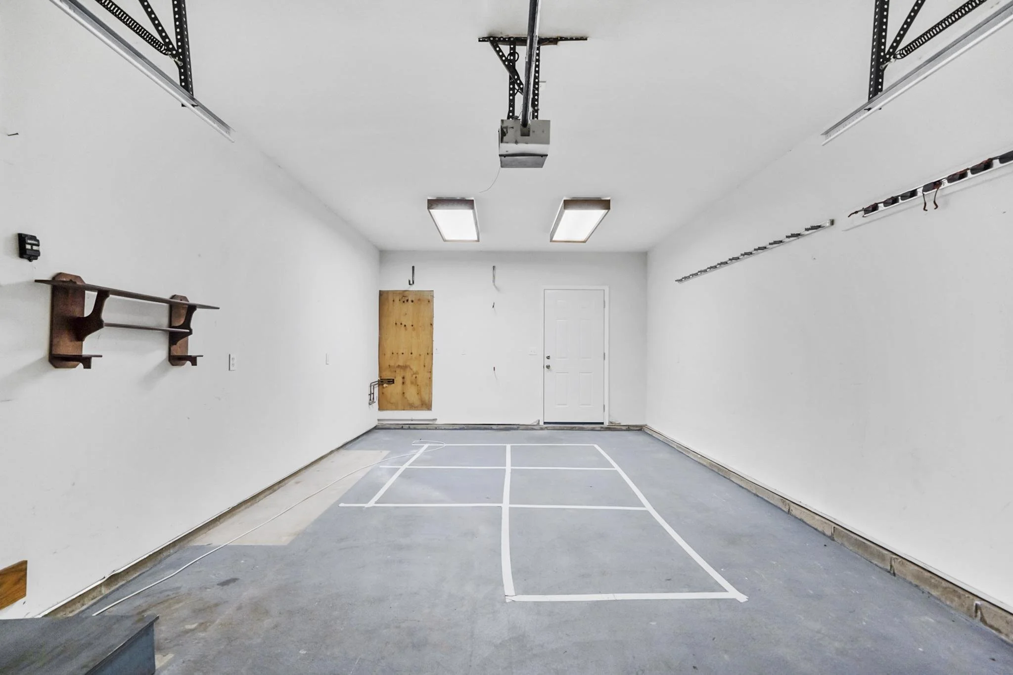 Empty garage with white walls, fluorescent ceiling lights, a wooden door and a marked sports court floor.