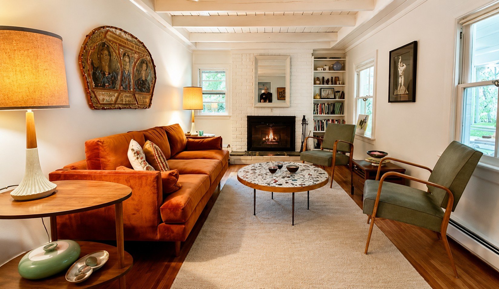 Living room with white brick fireplace, green armchairs, and orange sofa, wooden coffee table, and large windows.