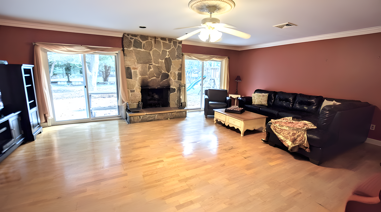 Living room with hardwood floors, stone fireplace, large sliding glass doors, and black leather sofa.