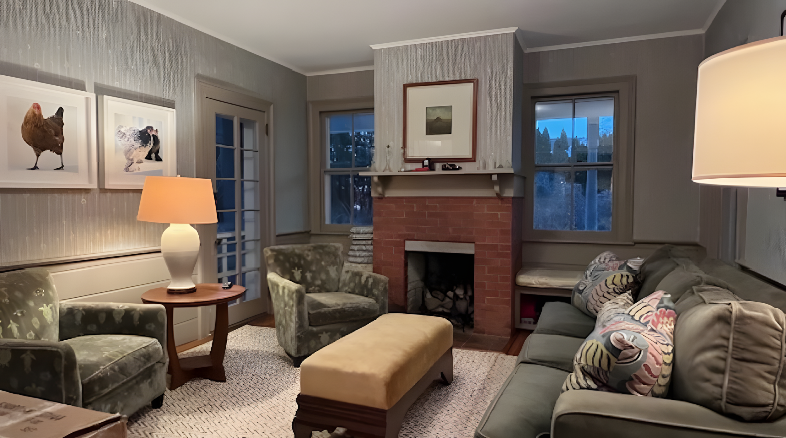 Living room with a fireplace, framed artwork, sofas, armchairs, lamps, and windows showing a dusk sky.