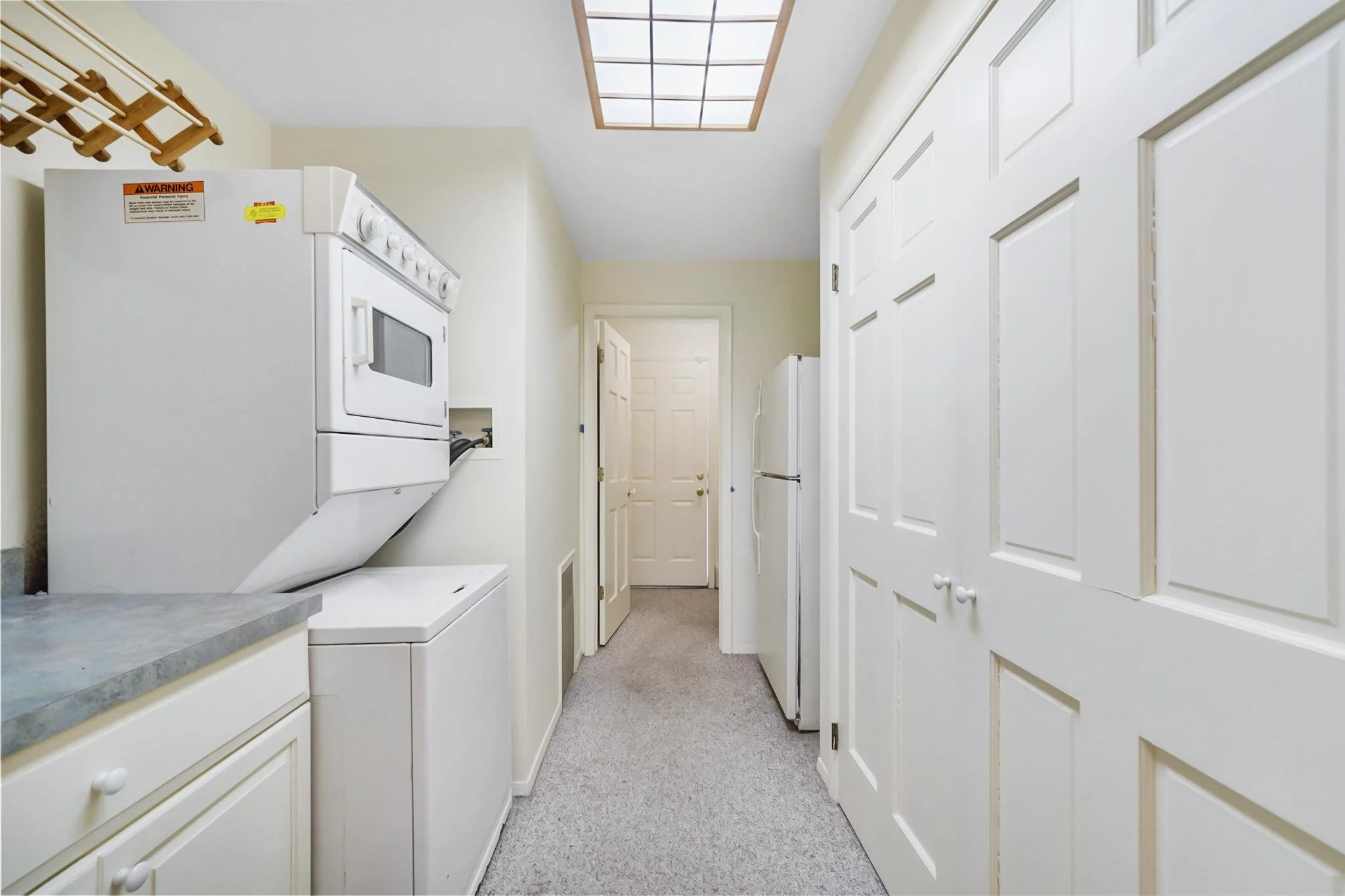 Laundry room with white cabinets, a washing machine, a dryer, and a closet with sliding doors, with a ceiling light fixture and a door at the far end.