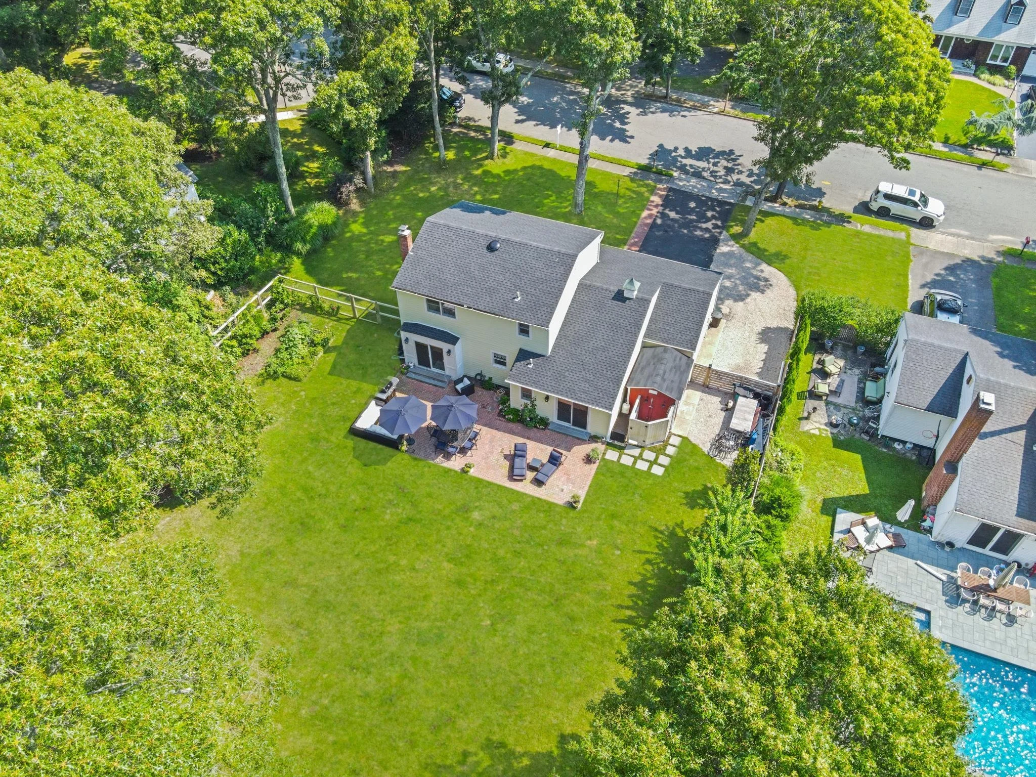 Aerial view of a residential neighborhood with green lawns, trees, houses, and parked cars on the street.