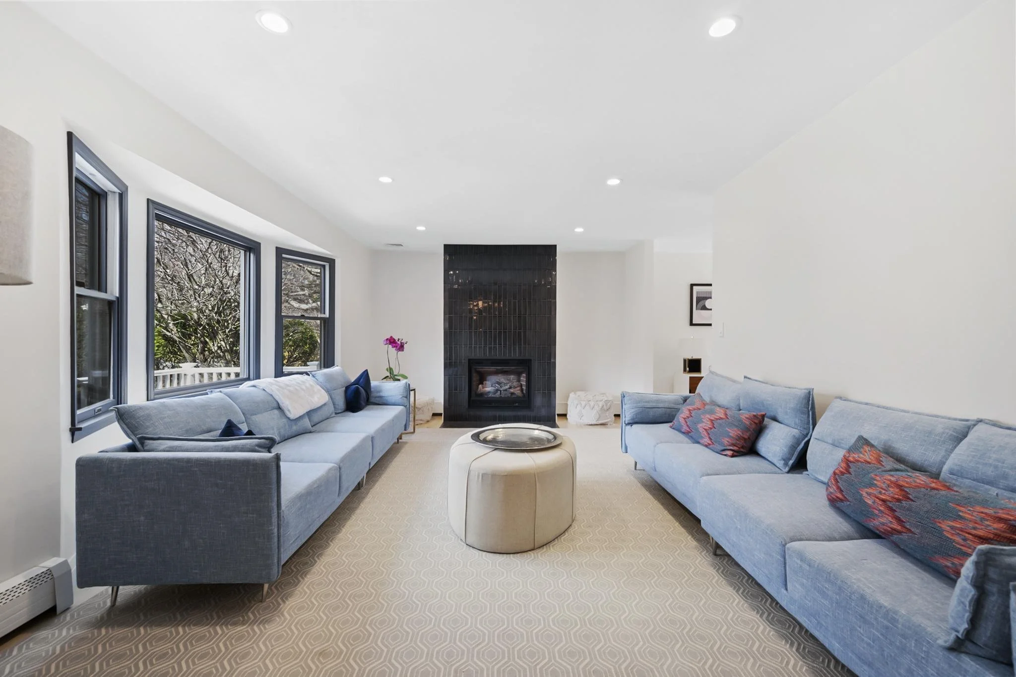 Living room with large blue sofas, a black fireplace, windows with snowy outdoor view, and decorative pillows and a pink flower.