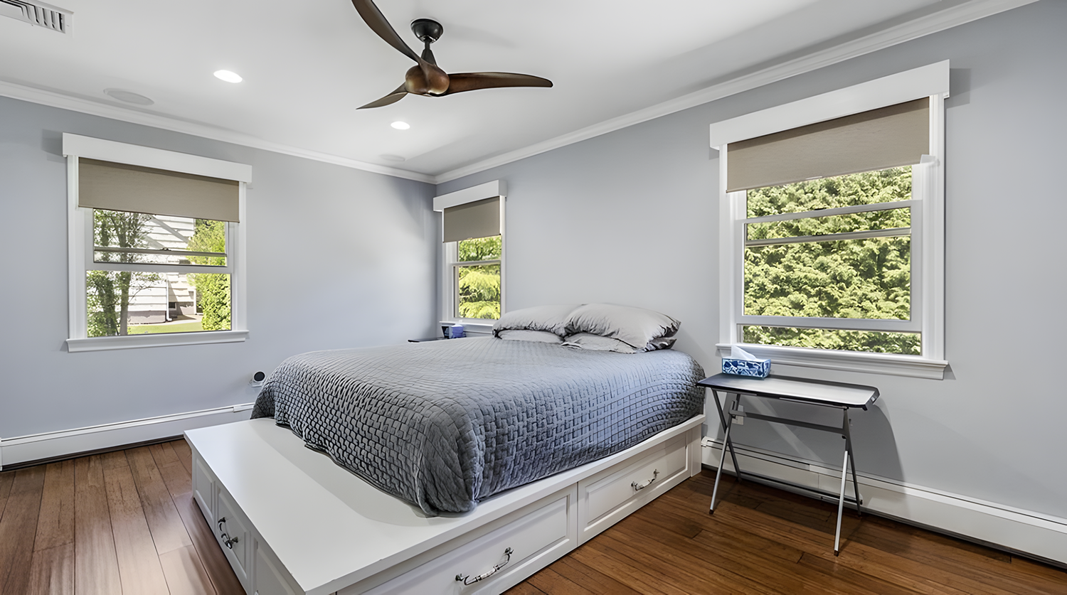 A bedroom with a bed, two windows, a nightstand, and a ceiling fan.