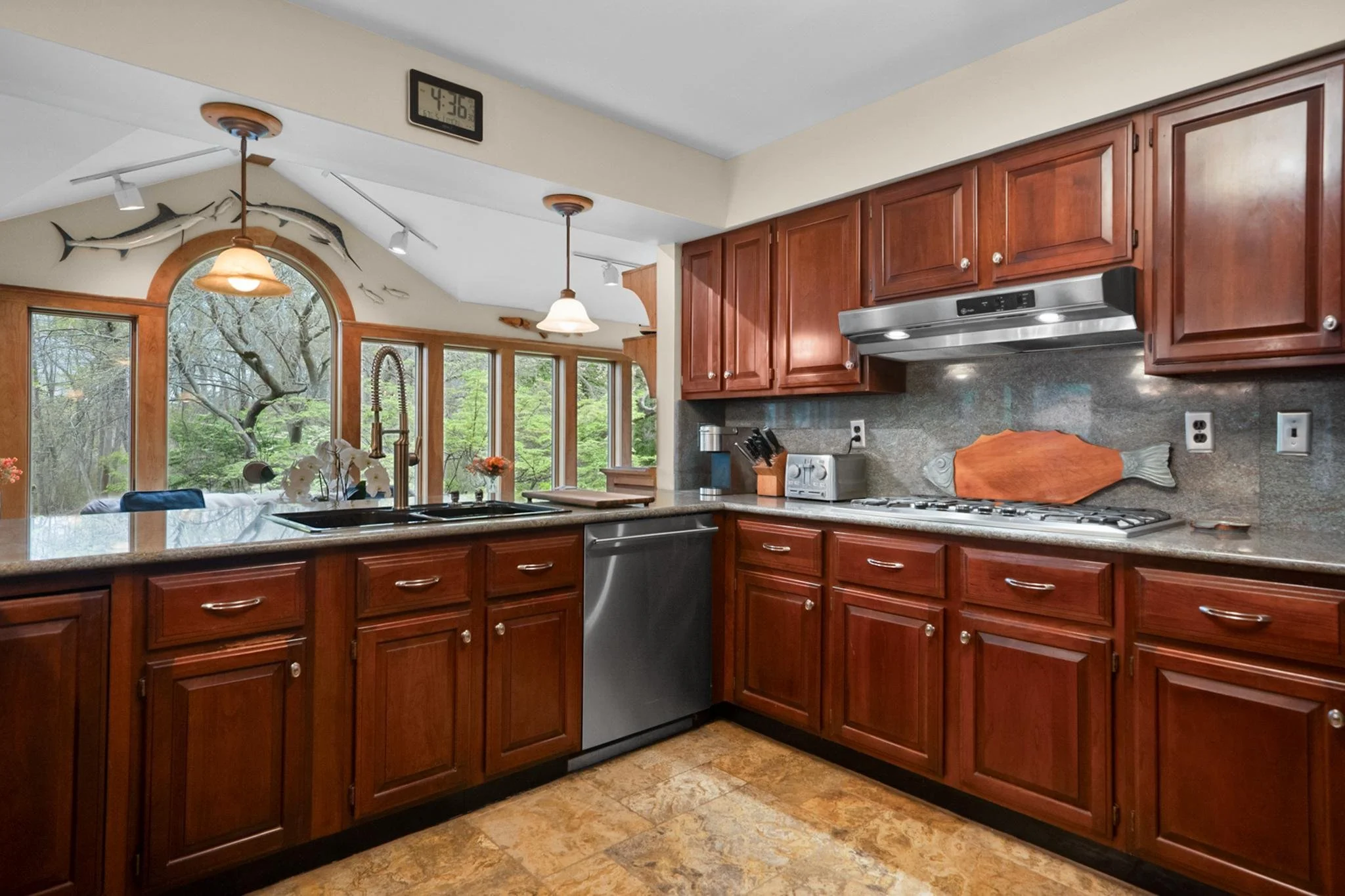 Kitchen with wooden cabinets, granite countertops, stainless steel appliances, a fish-shaped cutting board, and a window showing trees outside.