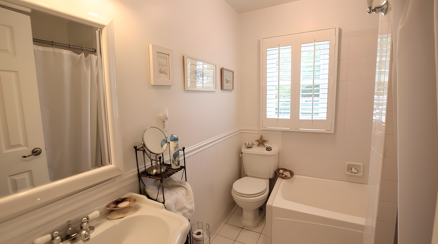 Bathroom with white sink, mirror, toilet, bathtub, window with blinds, and wall art.