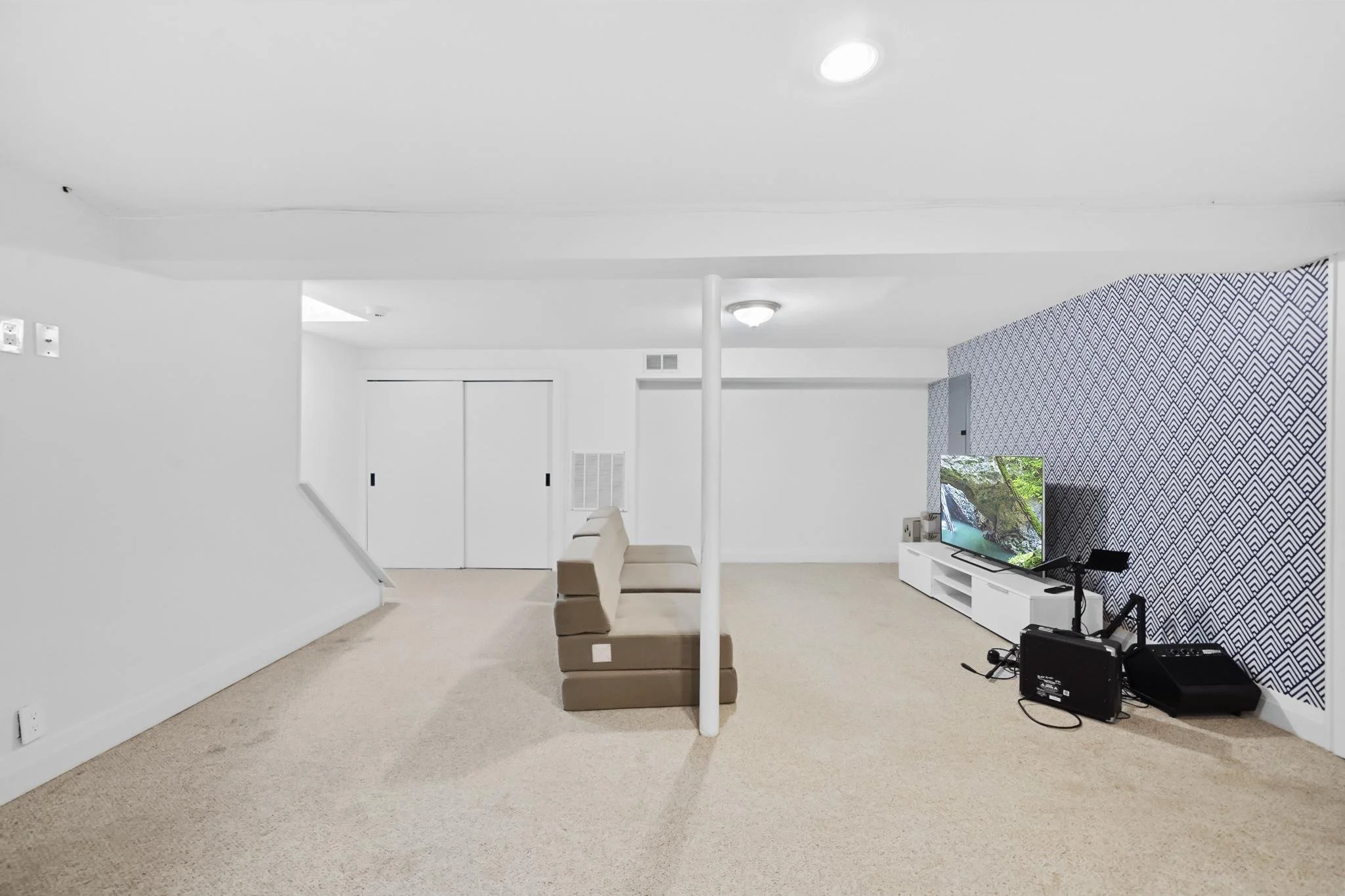 Living room with beige carpet, white walls, a TV on a white TV stand, a beige sofa, and a patterned accent wall.