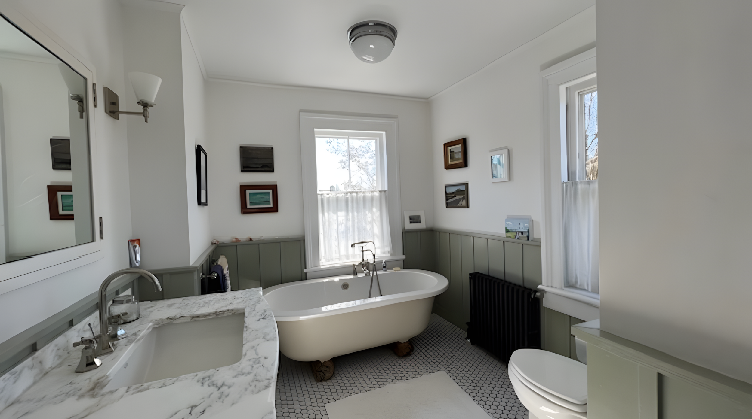 A bathroom with a clawfoot bathtub, a marble countertop with double sinks, several framed pictures on the walls, a window with curtains, and a ceiling light fixture.