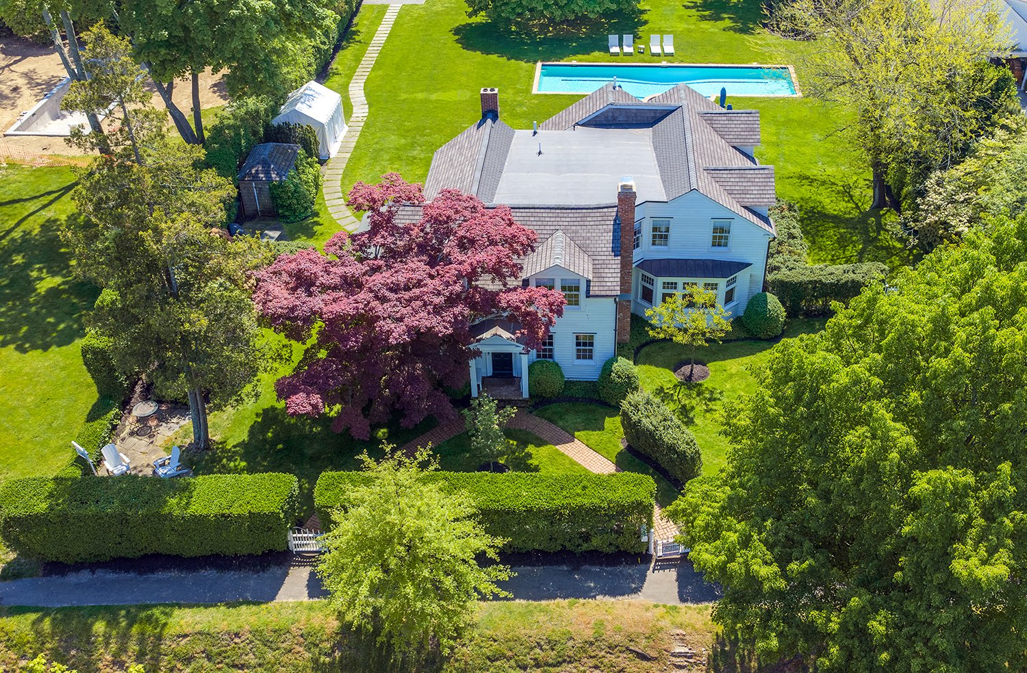 Aerial view of a large house with a backyard featuring a swimming pool, surrounded by lush green trees and manicured lawn.