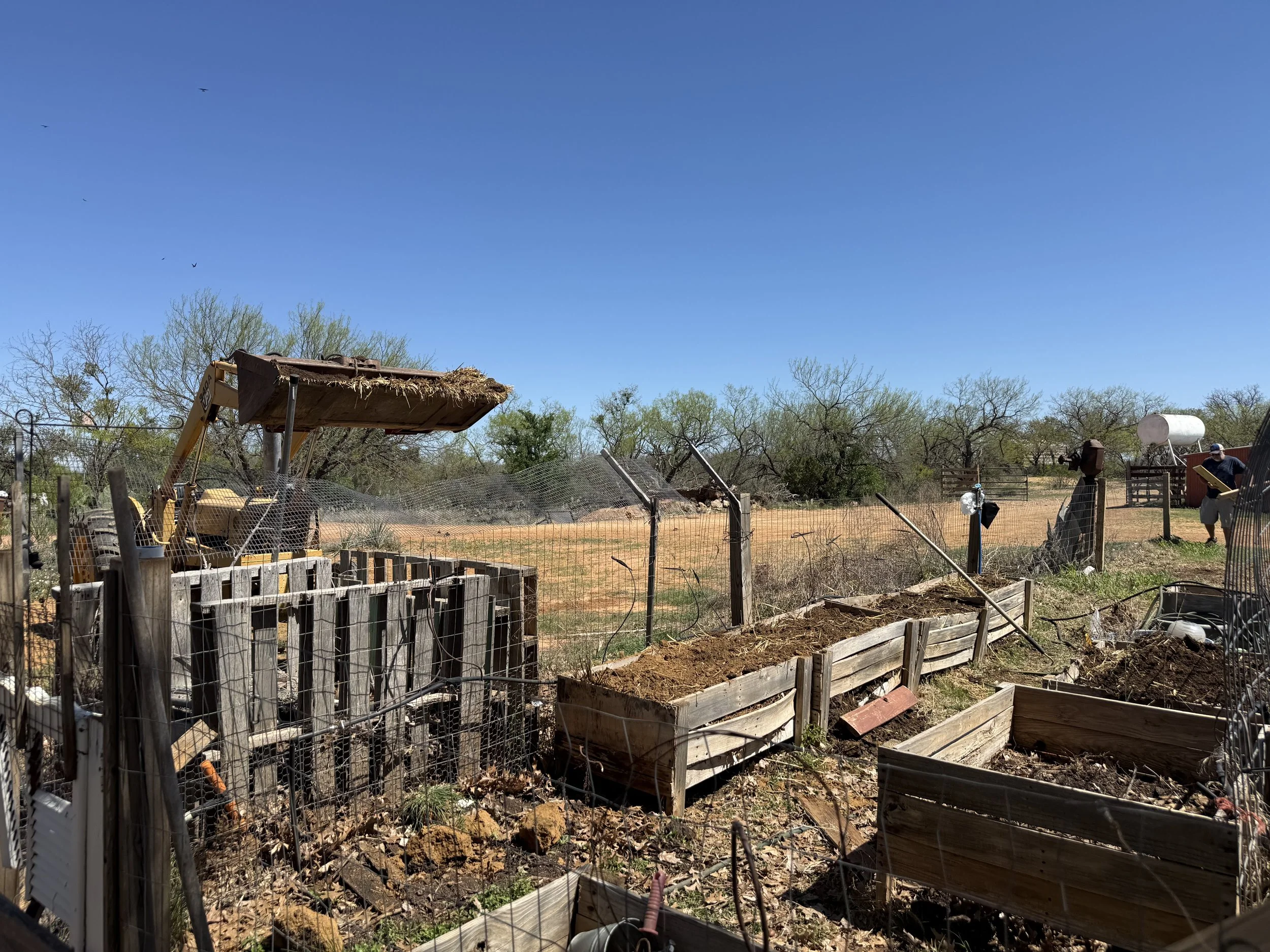 Raised garden beds being refreshed with compost and soil on a West Texas ranch, tractor adding organic material.