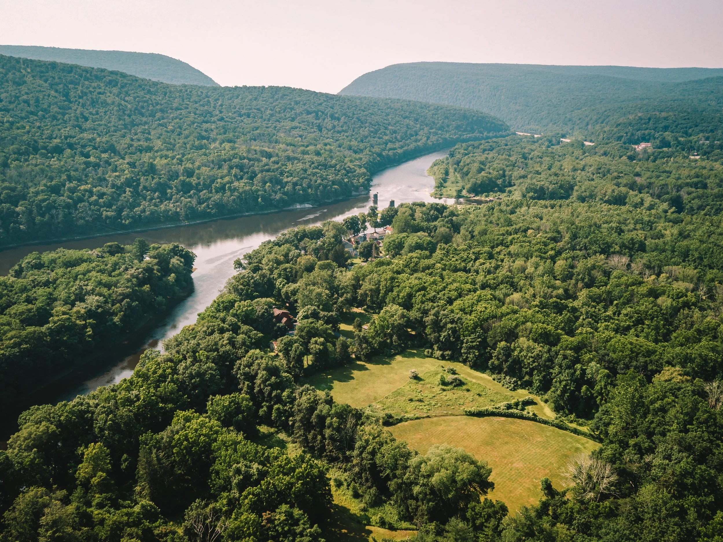 Aerial view of a winding river flowing through a green forested landscape with mountains in the background.