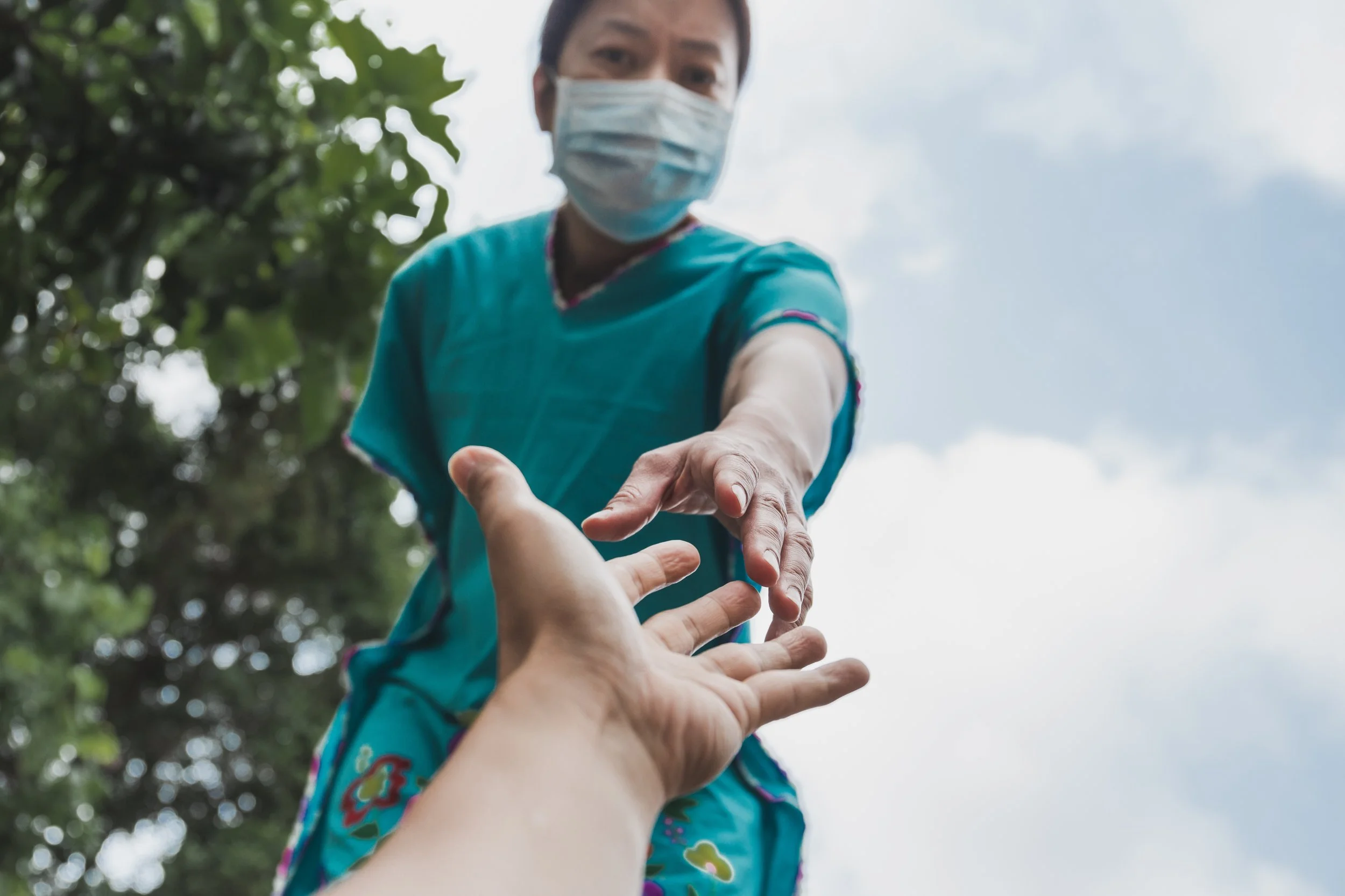 A healthcare worker wearing a mask outdoors reaching out to assist someone.