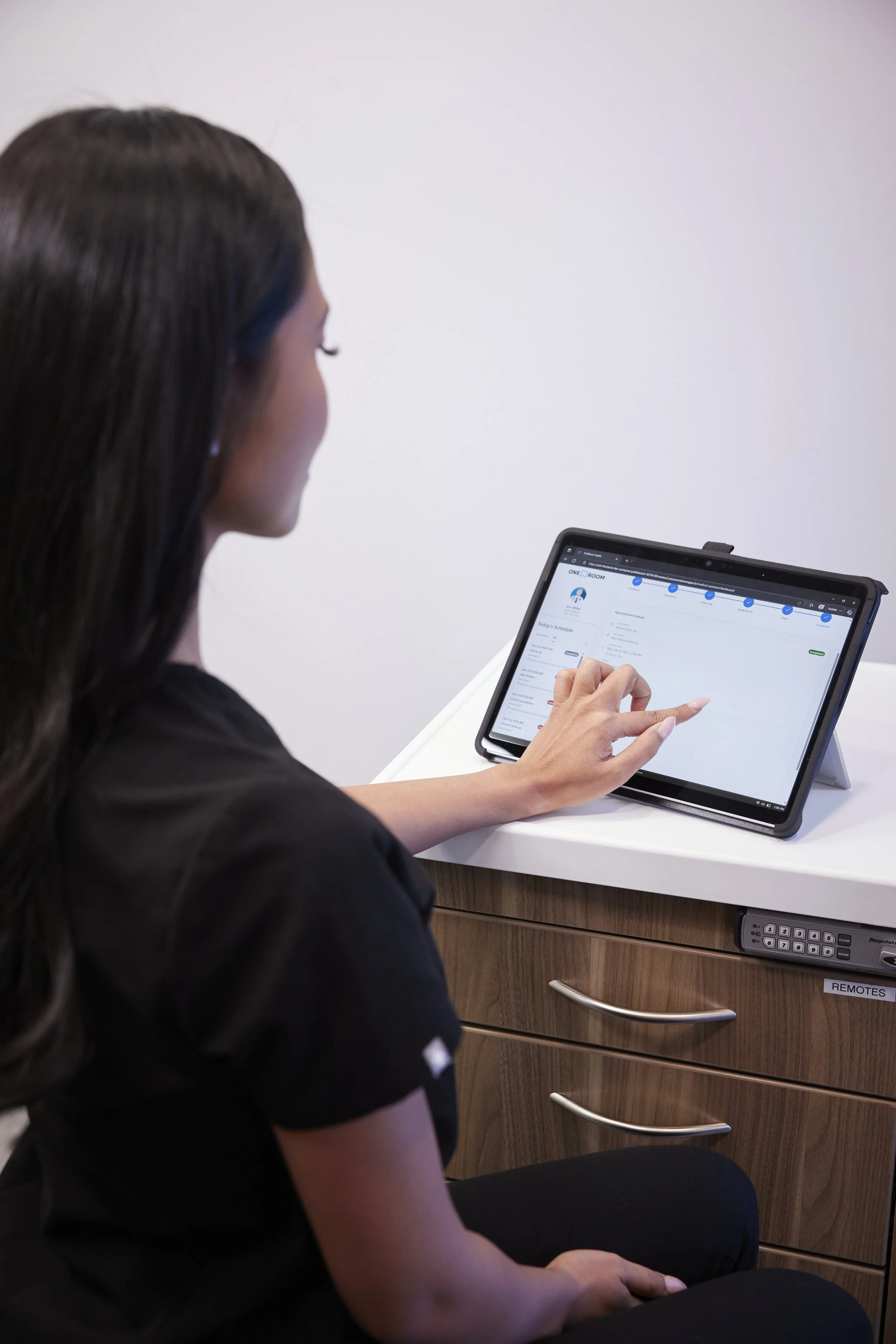 A woman in black scrubs using a tablet on a white desk.