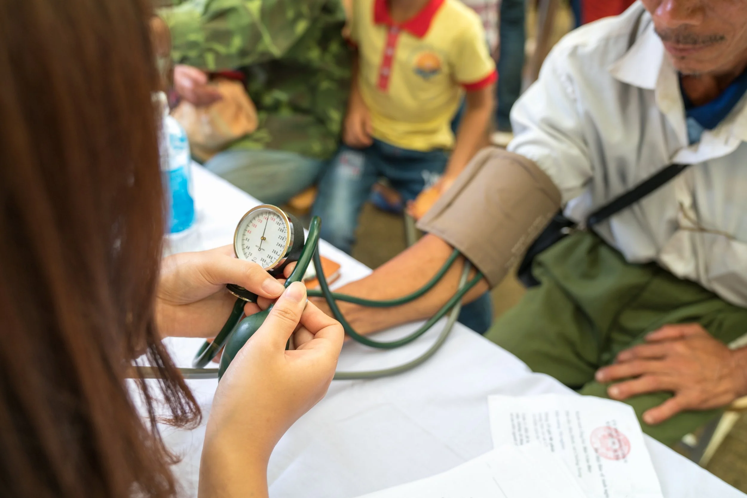 Medical professional measuring a man's blood pressure with a sphygmomanometer at a health check-up event.