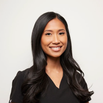 A woman with long black hair smiling at the camera, wearing a black top against a plain white background.
