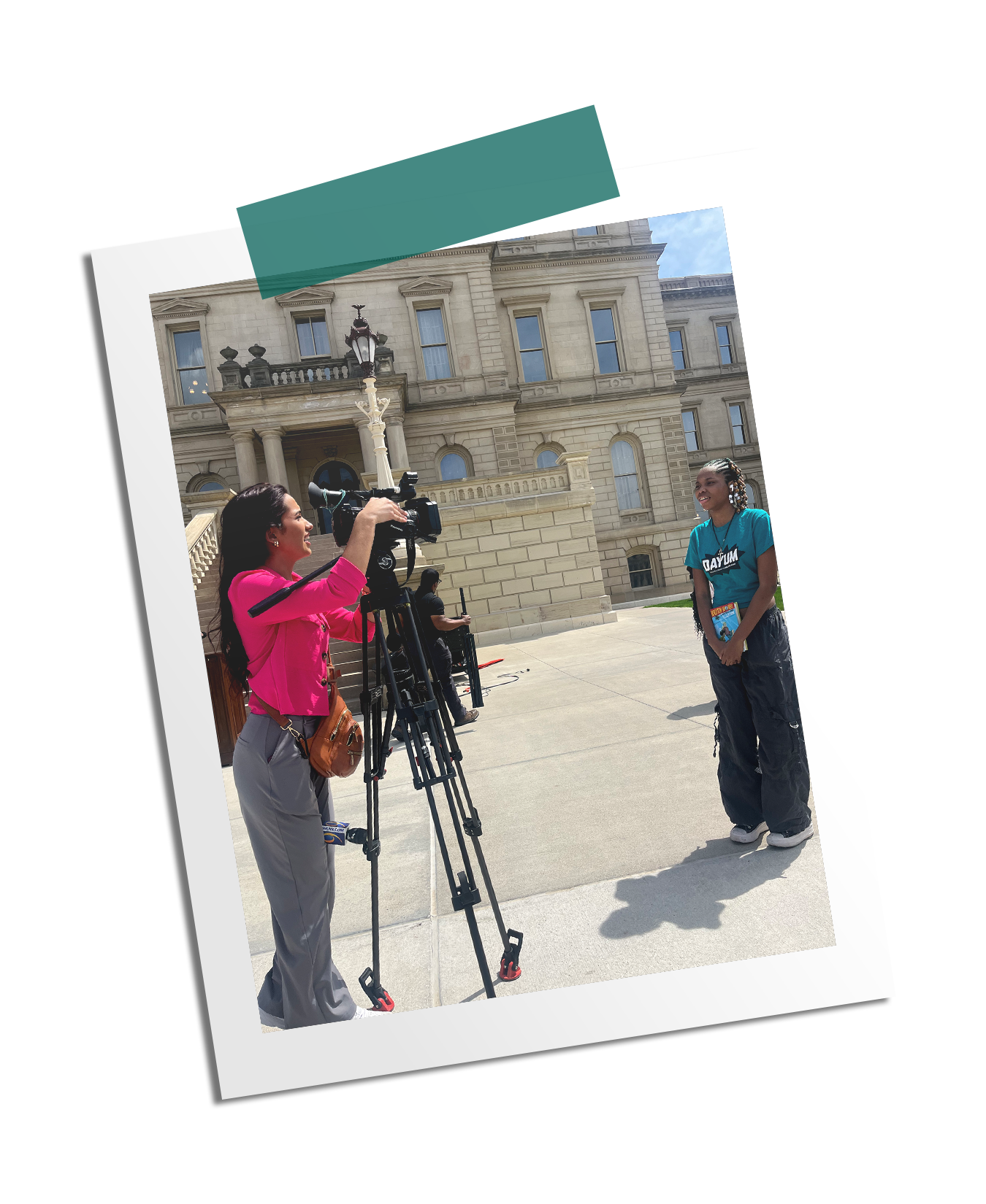 A woman filming a young girl on a camera outside a the Michigan State Capitol Building on a sunny day.