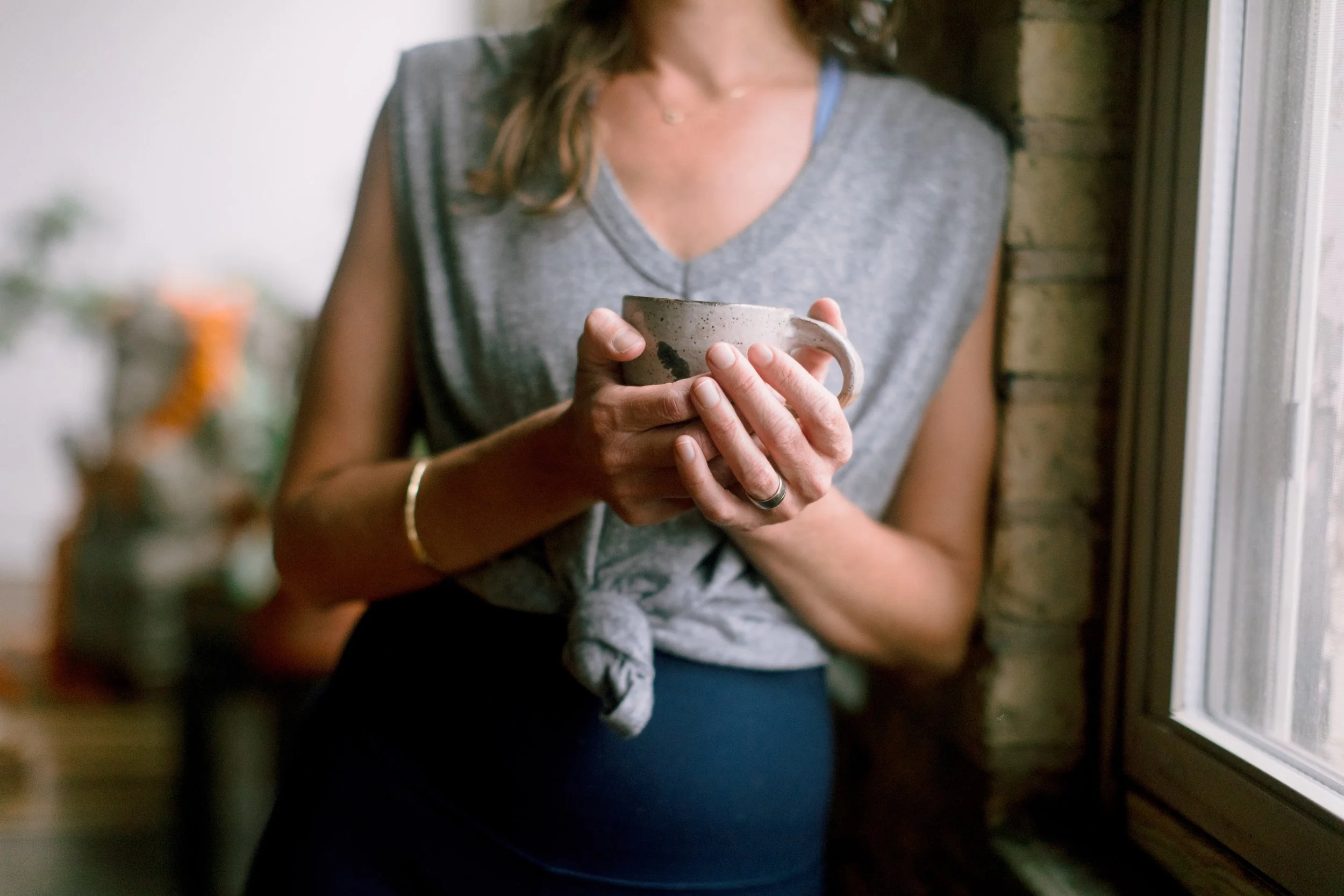 A woman holding a ceramic mug near a window.