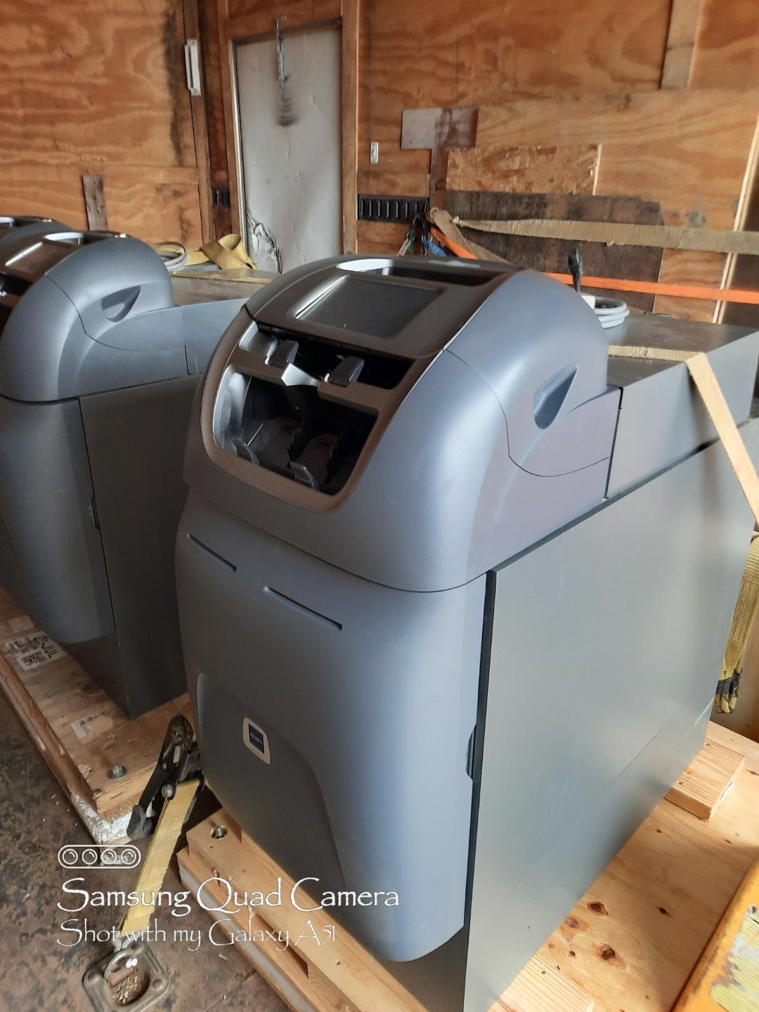 Two ice vending machines inside a wooden shed or garage, surrounded by tools and construction materials.