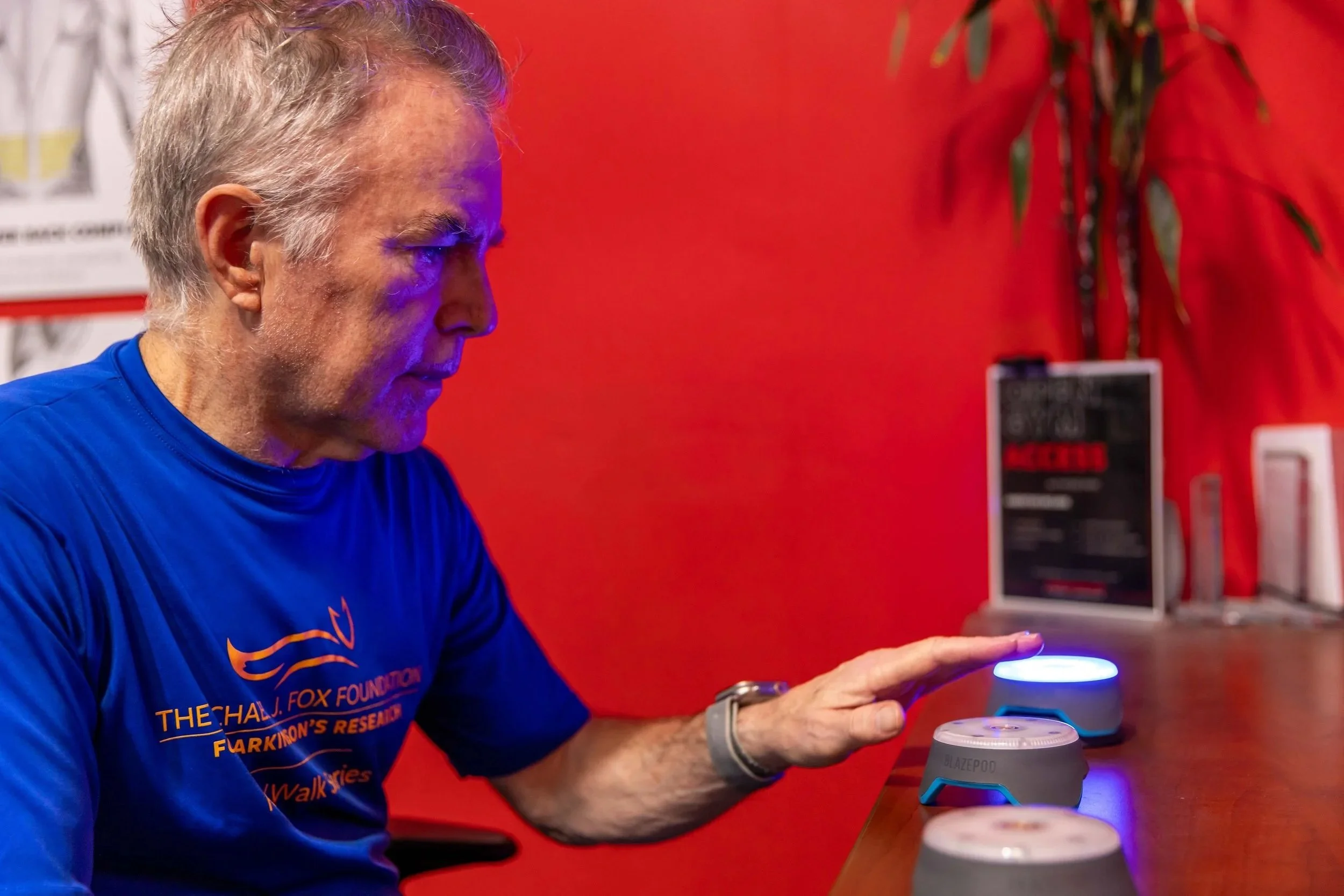 Man sits at a table and trains reaction time with Blazepods®, which are small circular lights that turn on and off. One is lit up. The wall behind him is red.