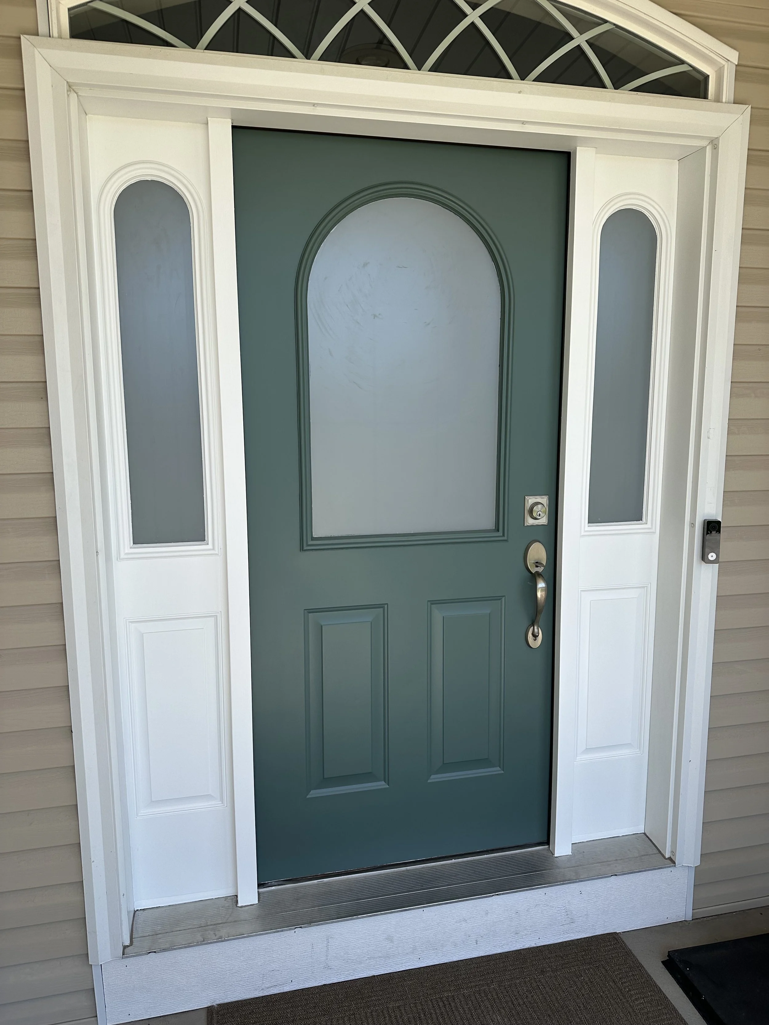 Front door painted in teal with frosted glass panels on either side and an arched top transom window above, surrounded by white trim.
