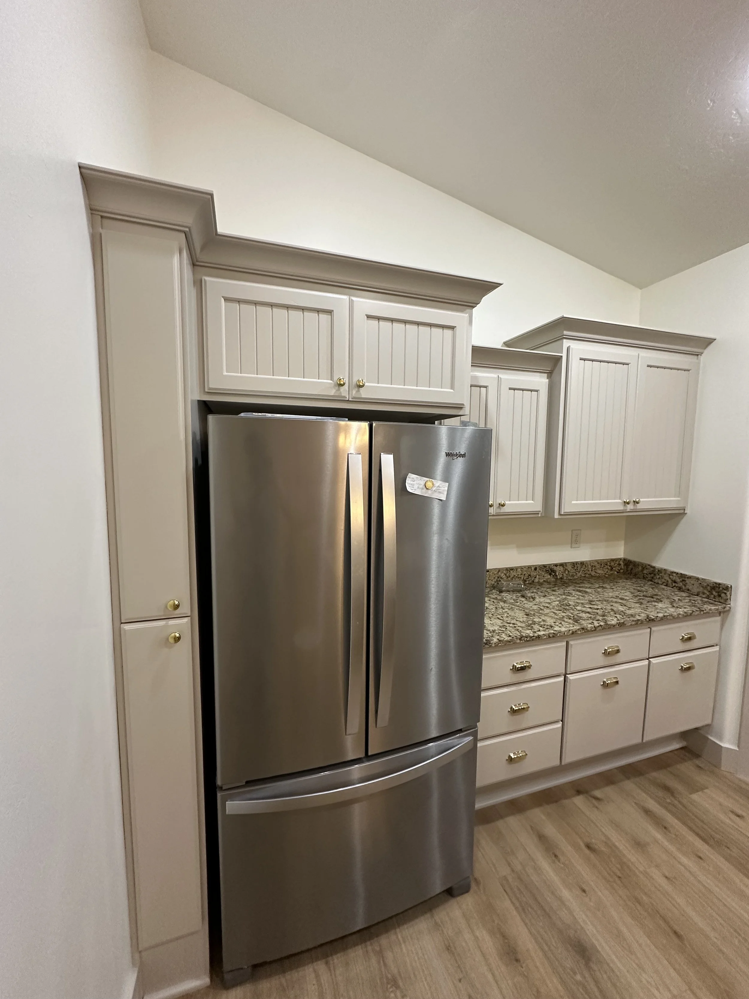 Stainless steel Whirlpool refrigerator in a kitchen with beige cabinetry, granite countertops, and wood flooring.