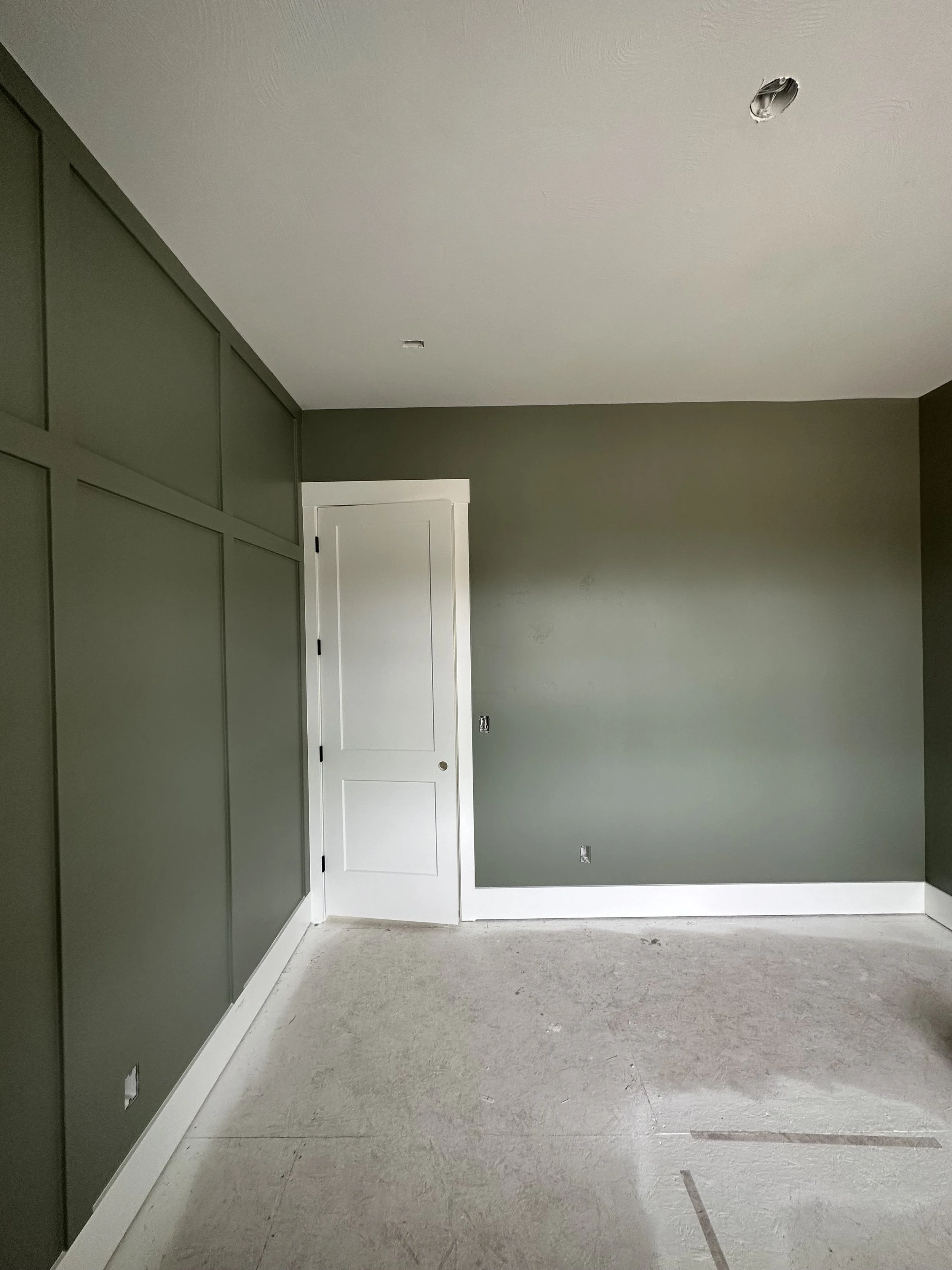 Empty room with green painted walls, a white door, electrical outlets and uninstalled fixtures on the ceiling, and a concrete floor.