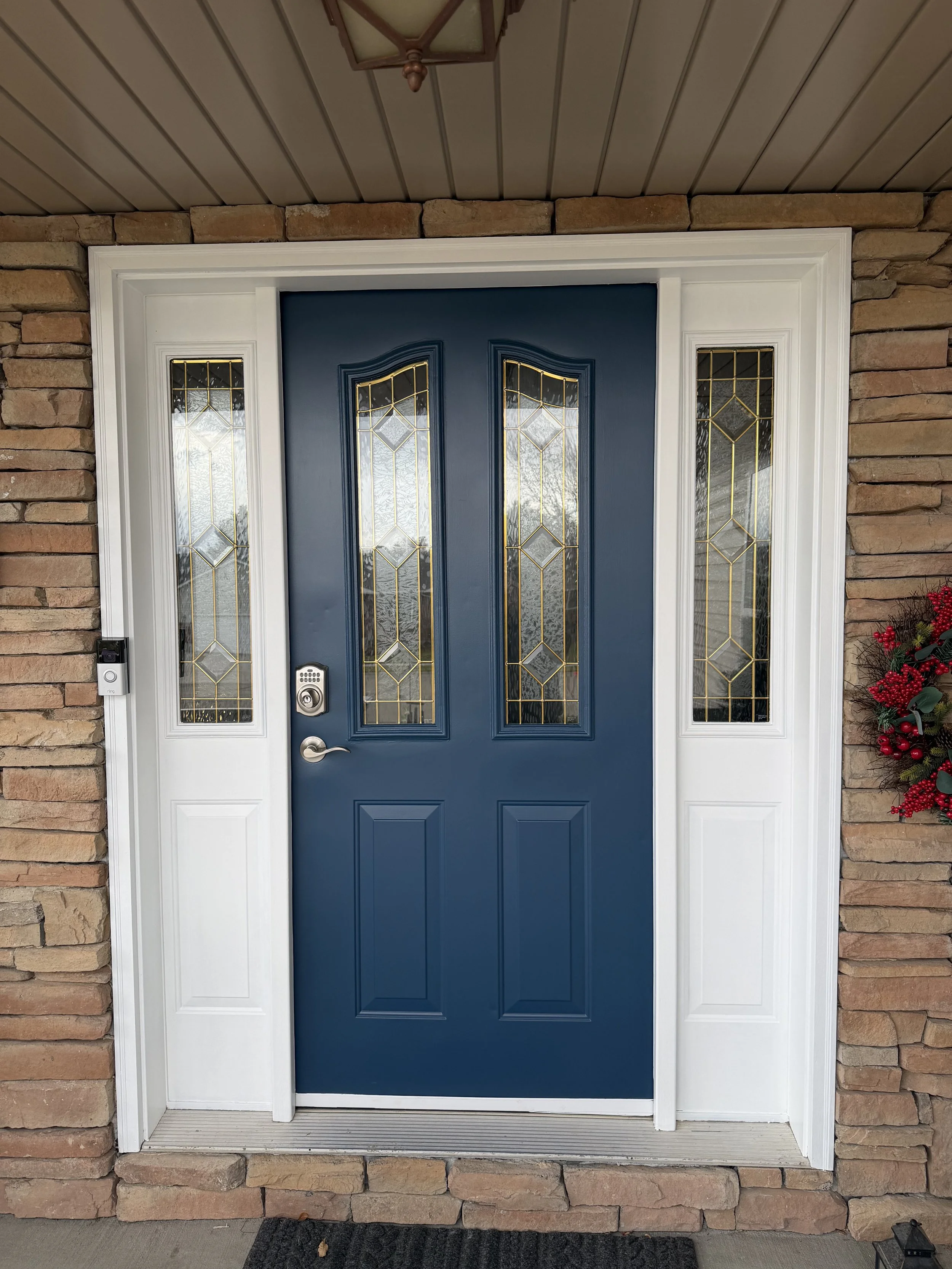 Front door with a blue door and glass panels, white frame, brick wall, and a decorative ceiling light