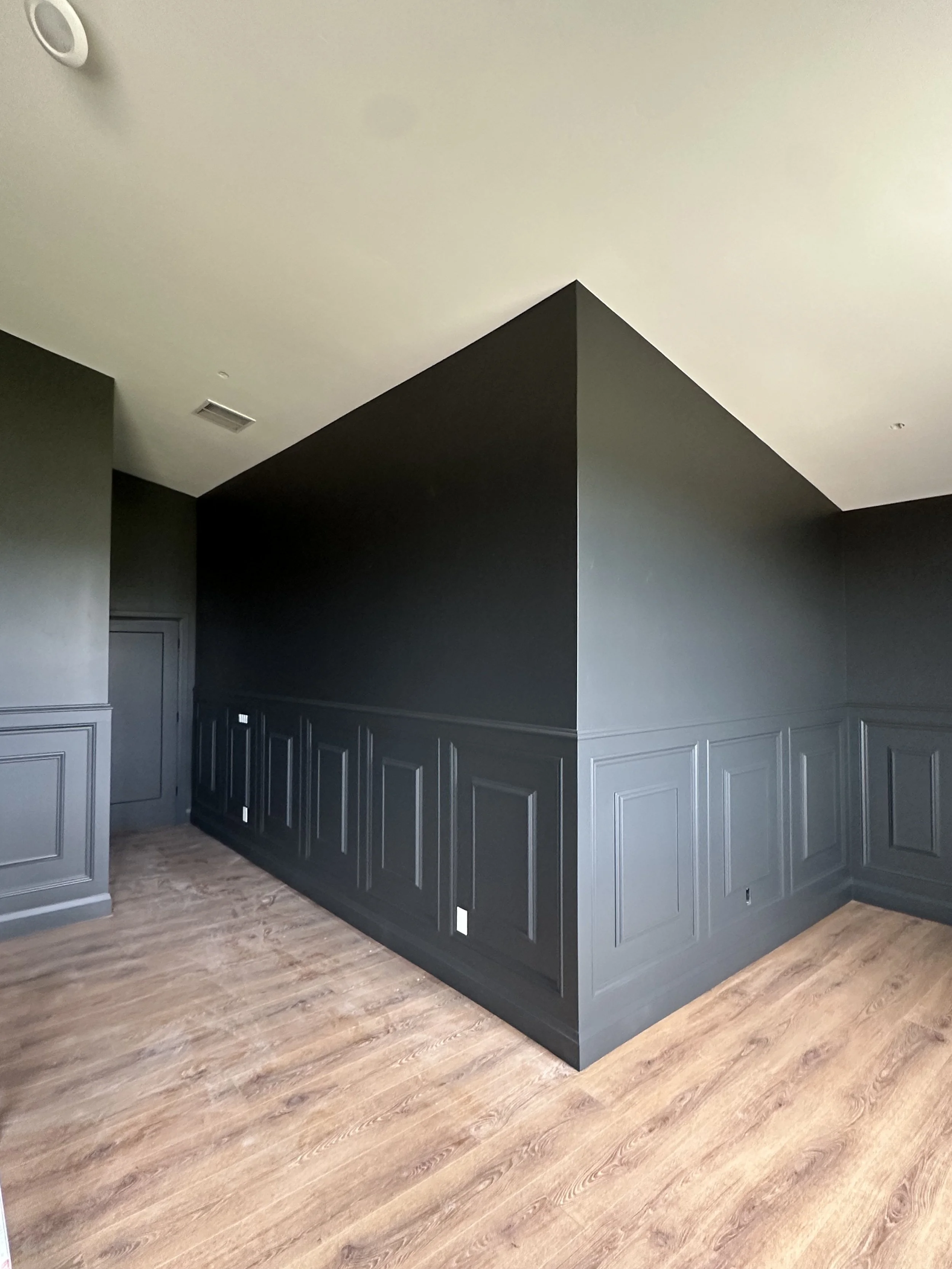Modern interior room with dark gray paneled lower walls, light hardwood flooring, and a beige ceiling.