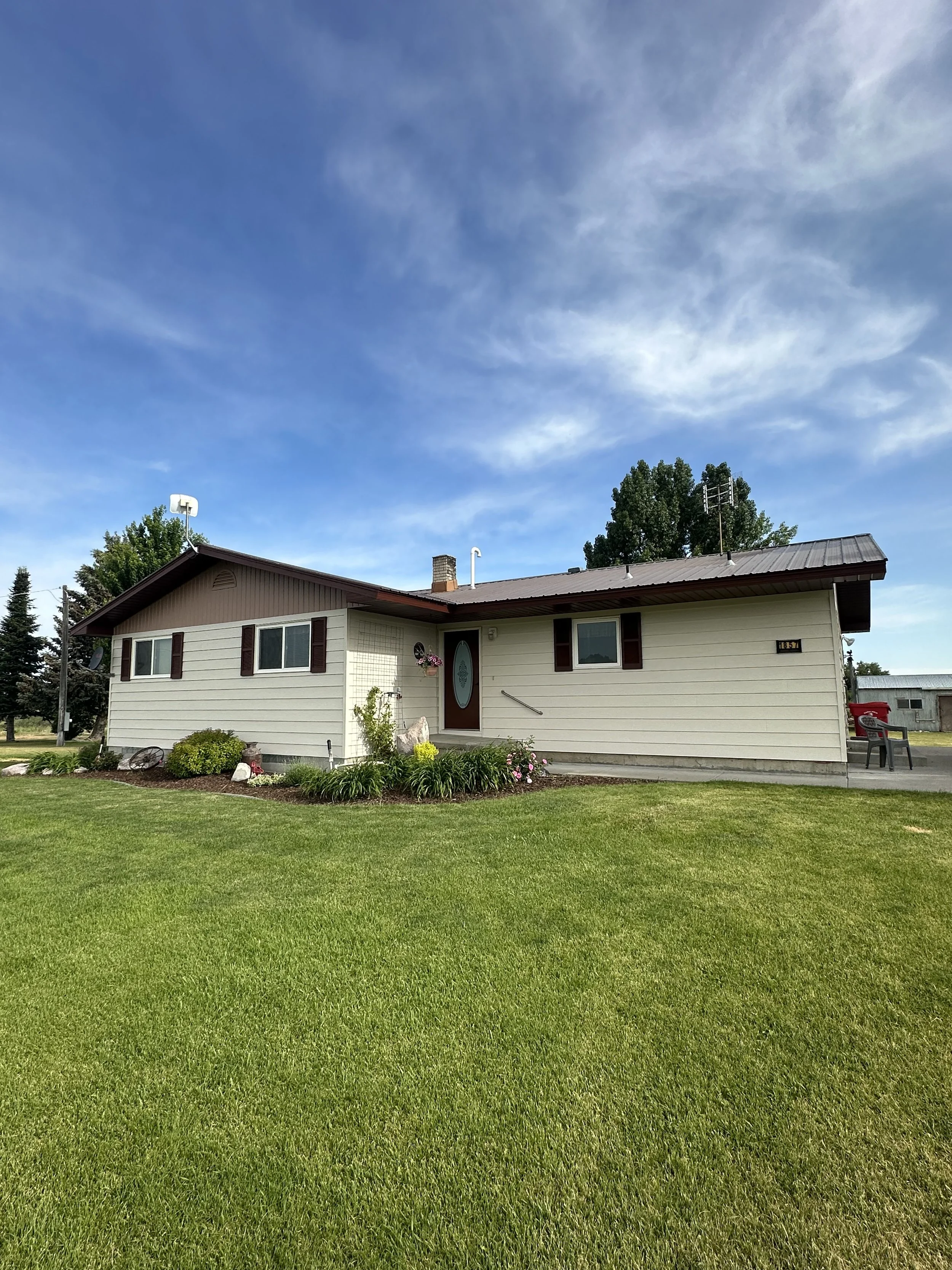 Front view of a single-story house with a manicured lawn, garden, and a clear blue sky.