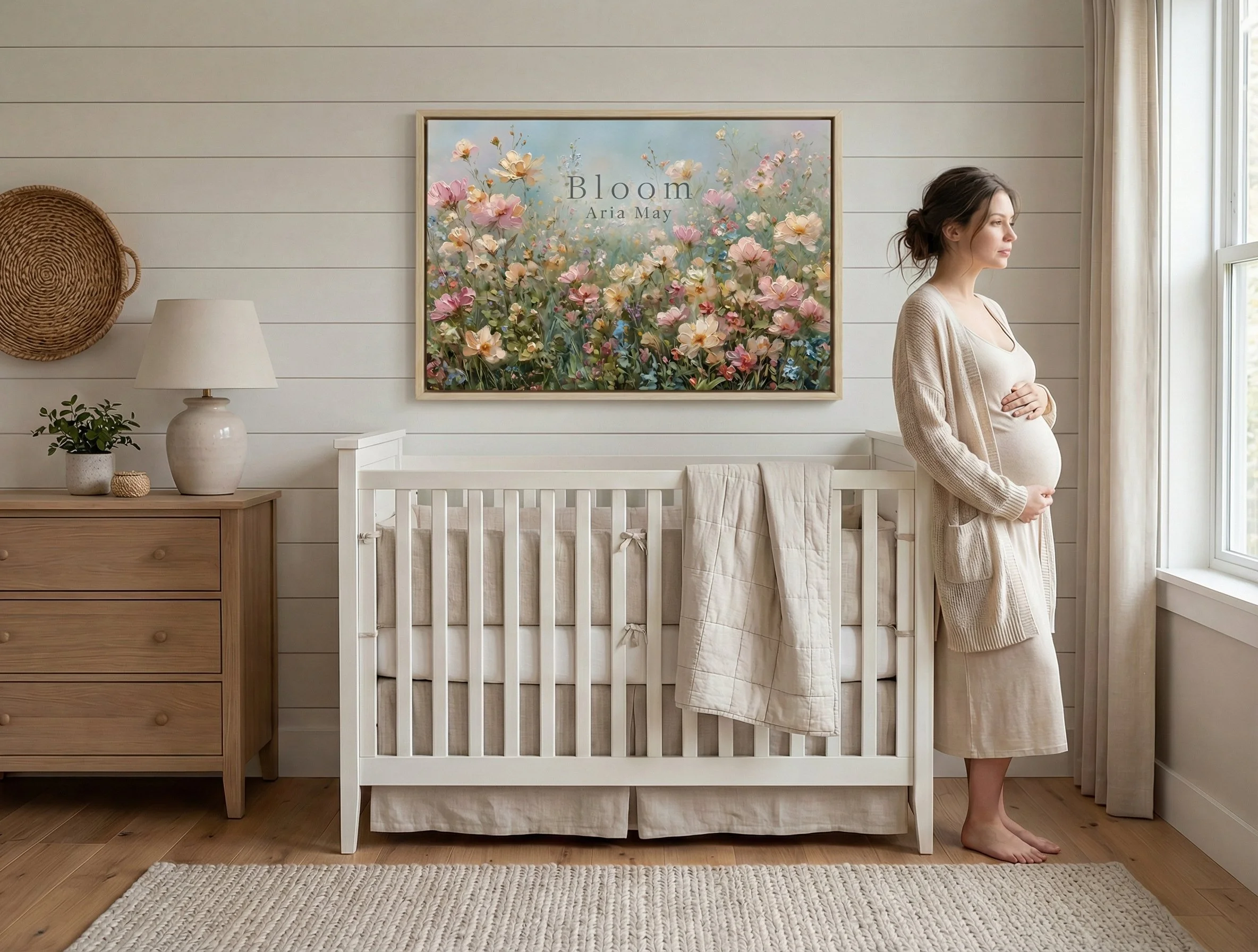 Pregnant woman standing by the window in a light-colored nursery with a white crib, a wooden dresser, a table lamp, and floral art on the wall.