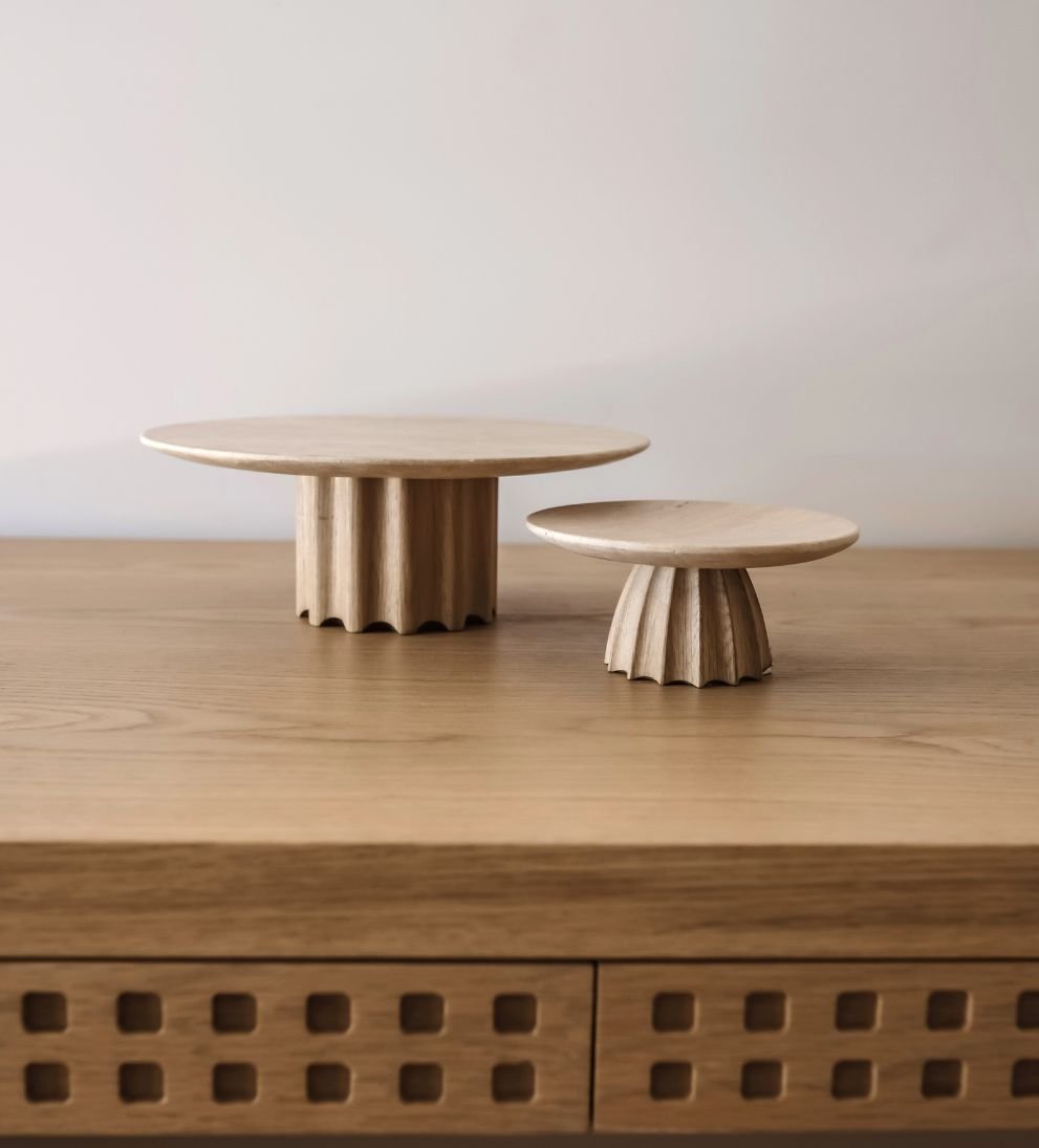 Two beige wooden decorative objects with scalloped bases and flat circular tops placed on a wooden surface.