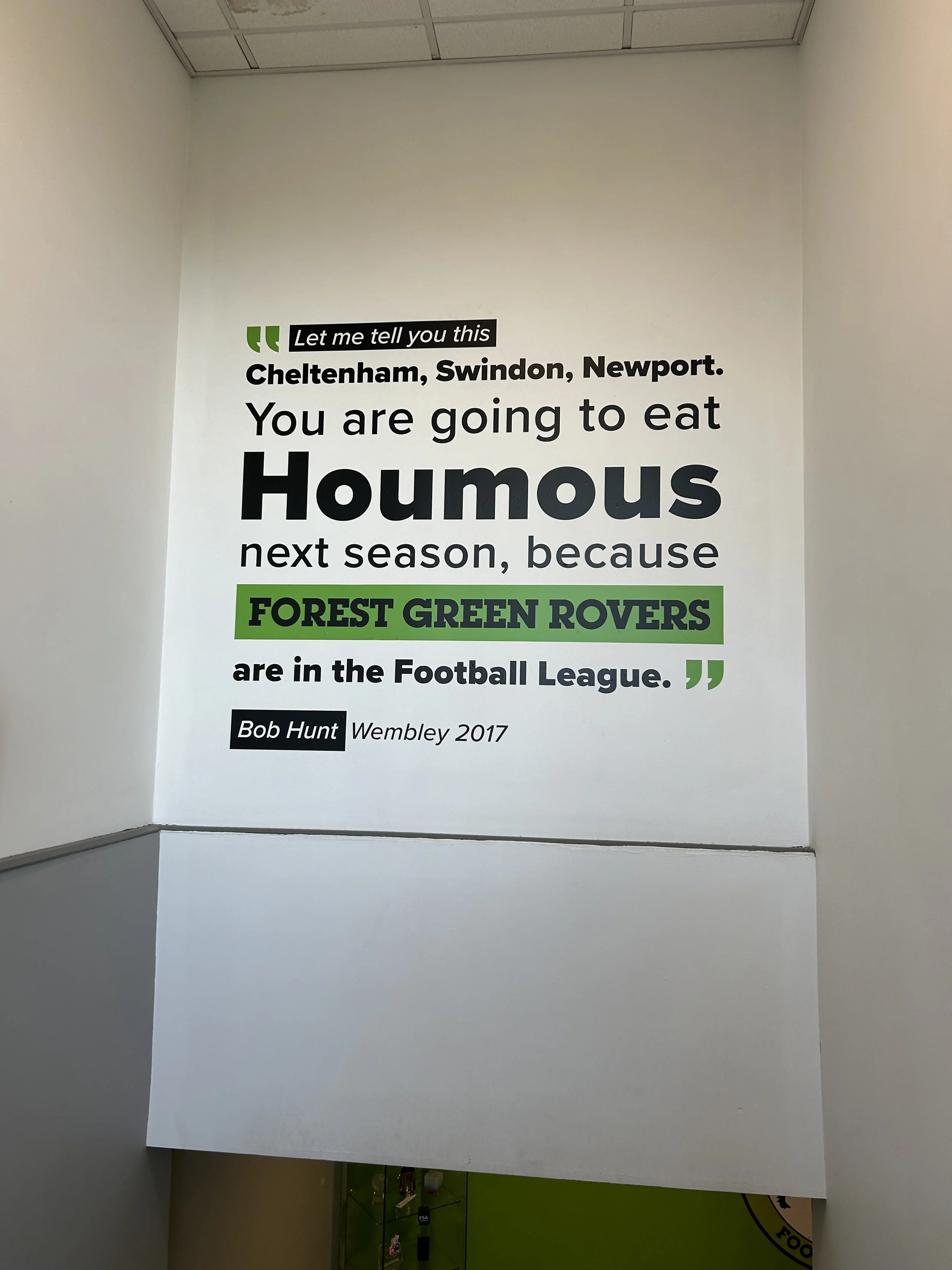 Wall with a quote about eating hummus, mentioning Cheltenham, Swindon, Newport, and Forest Green Rovers, attributed to Bob Hunt and dated Wembley 2017.
