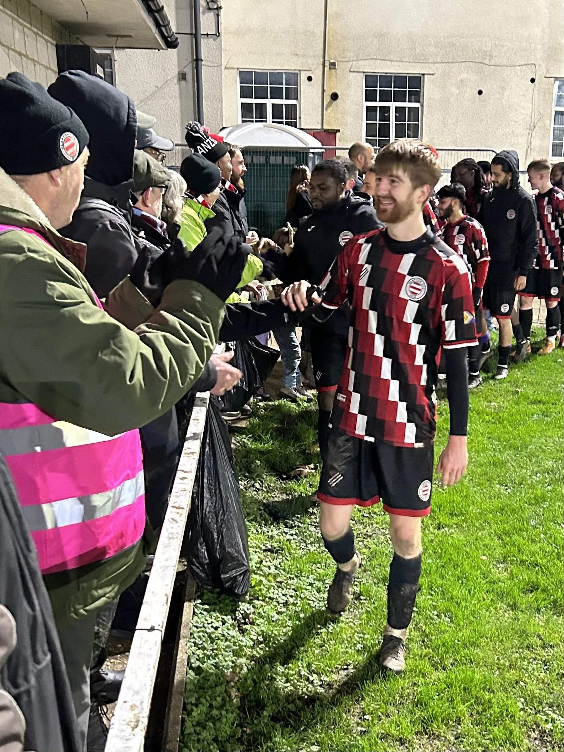 Soccer player in a colorful uniform shaking hands with fans behind a barrier