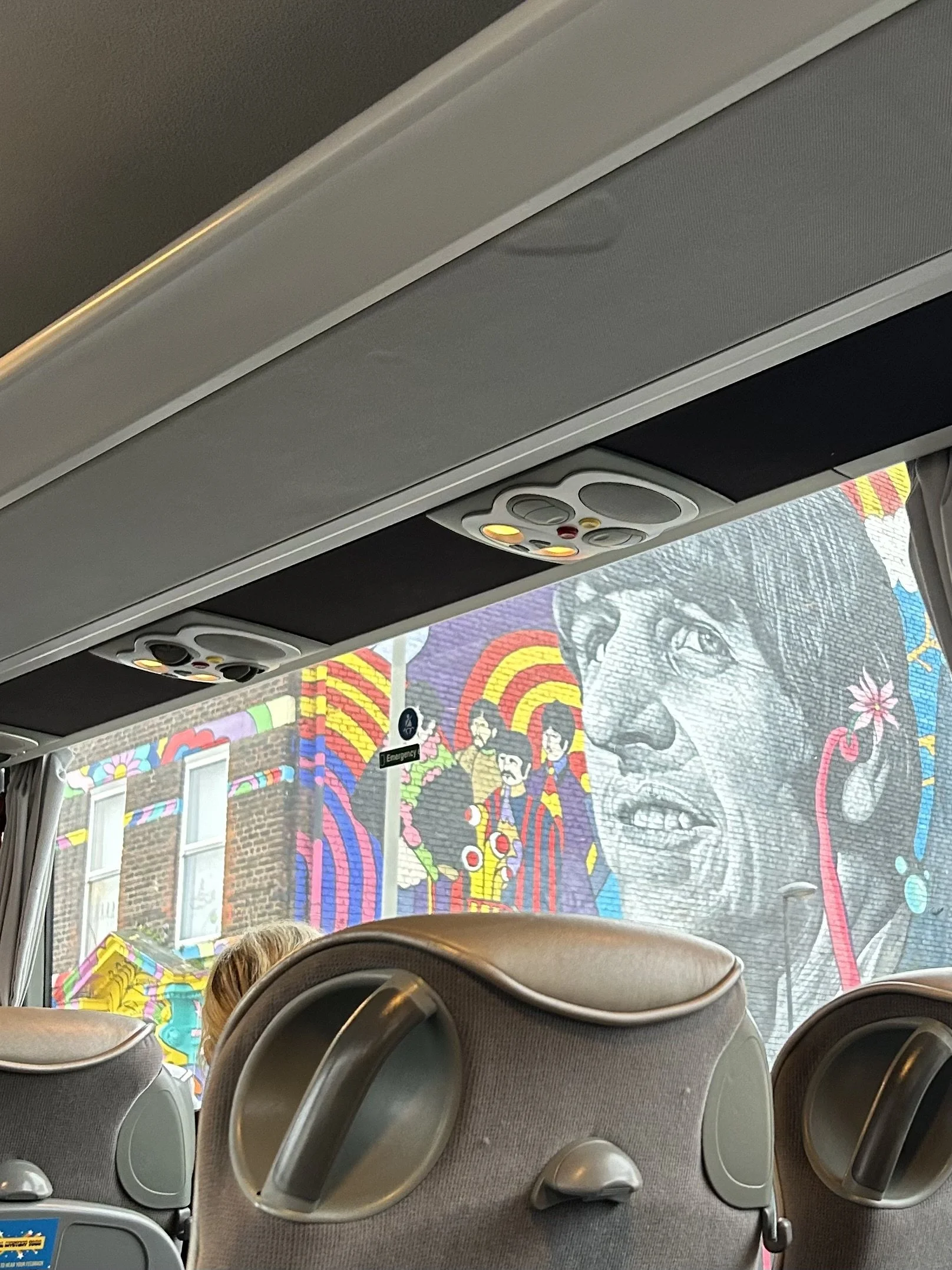 Colorful mural of a woman's face and several smaller figures on a building outside a bus window.