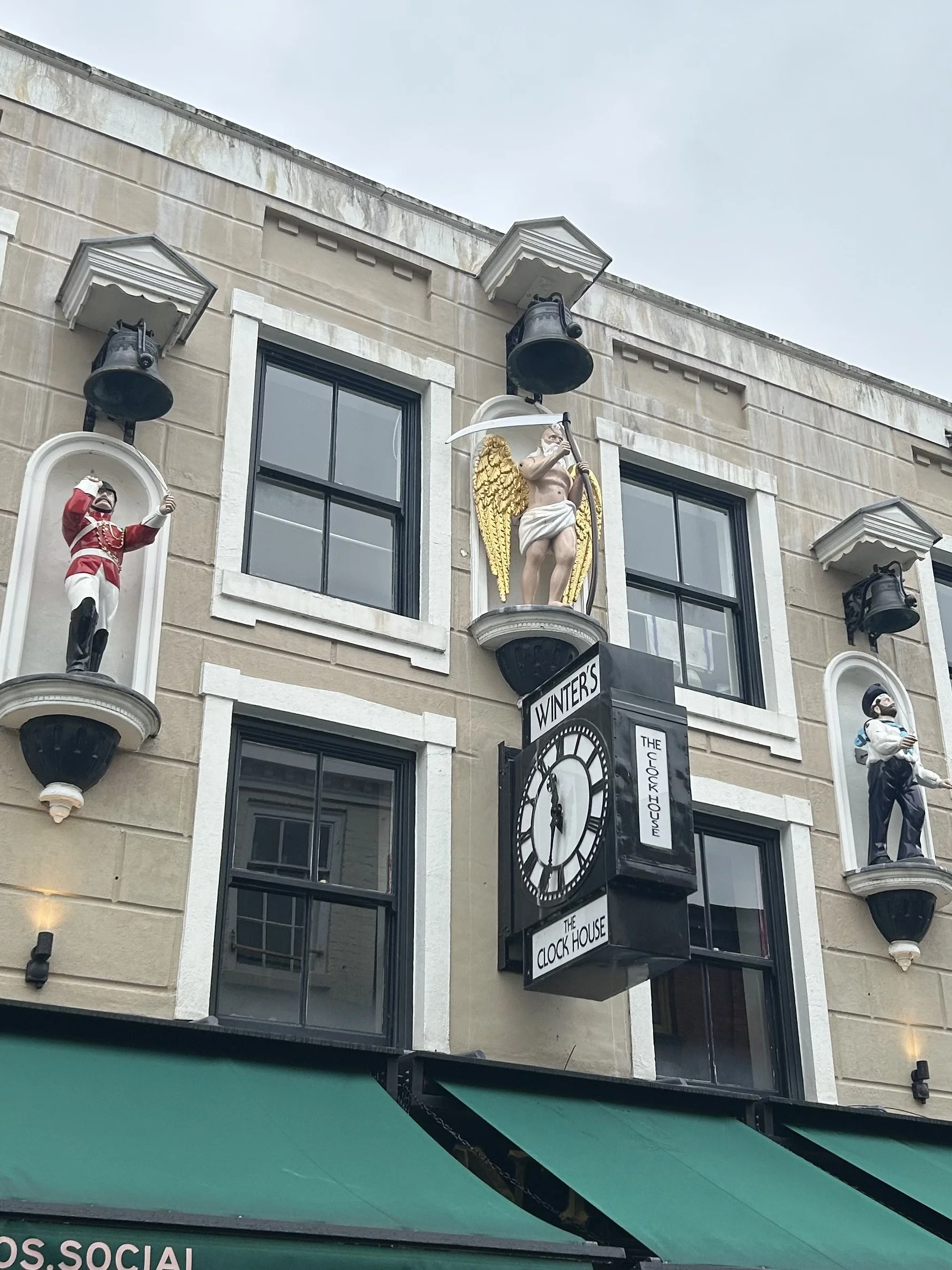 The facade of a building featuring a clock with the words 'Winter's The Clock House', surrounded by four decorative sculptures of musicians and characters, each in a separate niche.