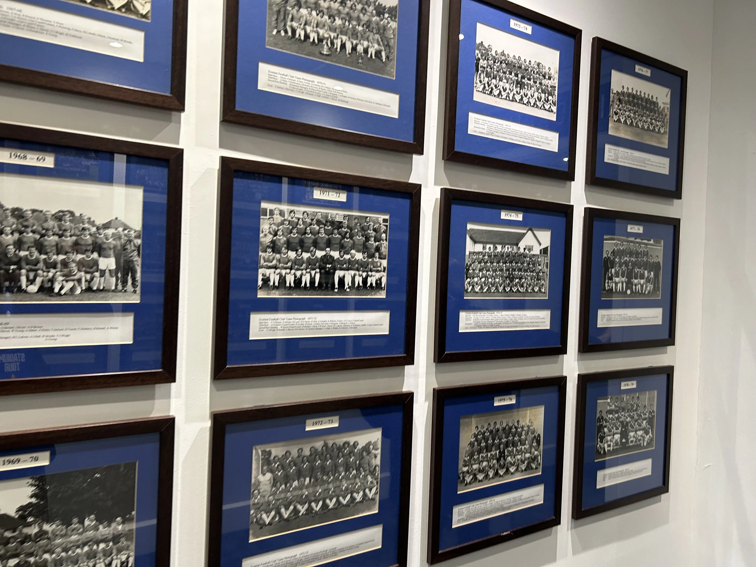 Gallery of framed historical team photographs with blue backgrounds, arranged on a white wall.