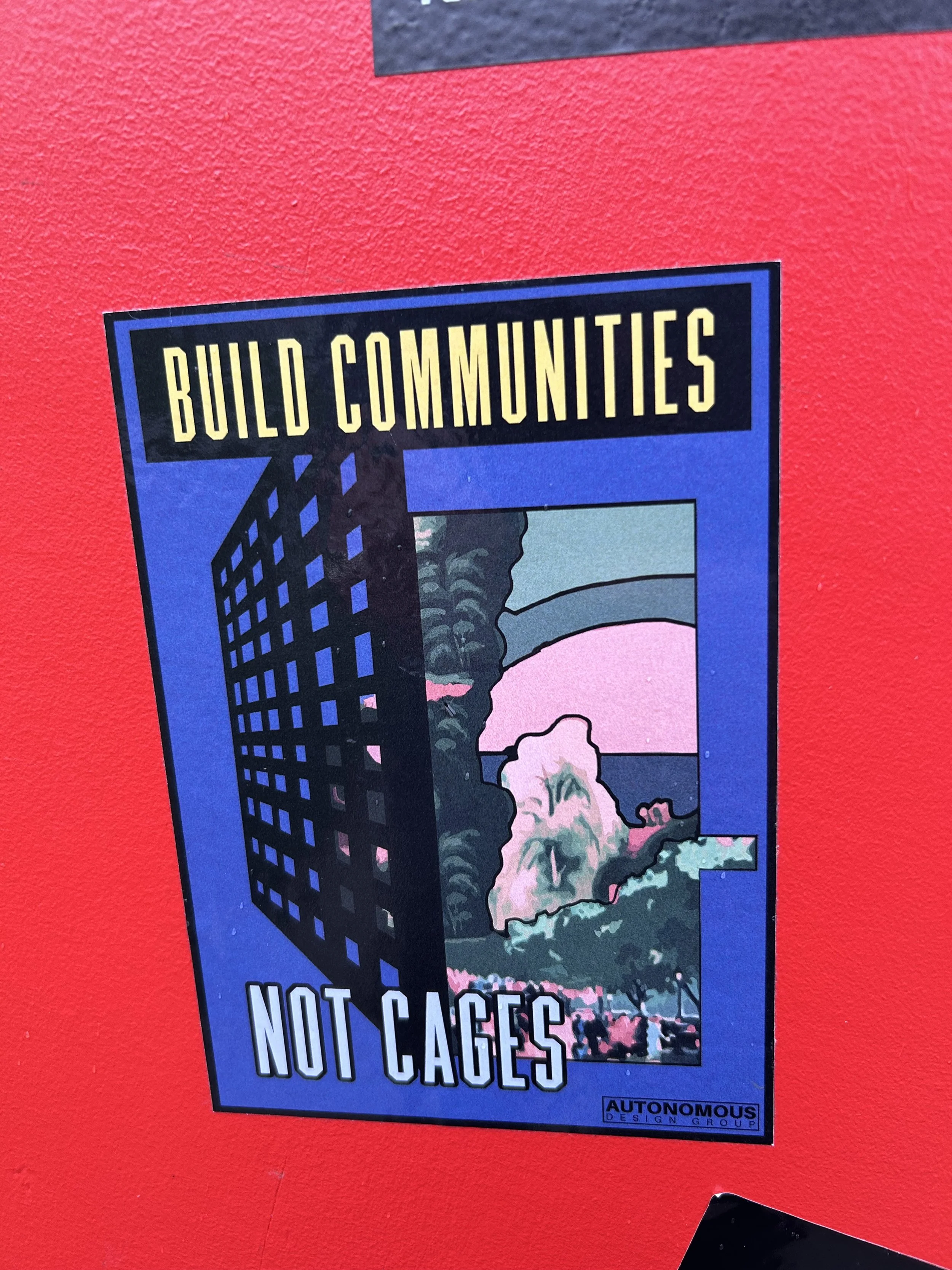 Poster with a graphic of buildings and trees, reading "Build Communities Not Cages" in bold letters, on a red background.