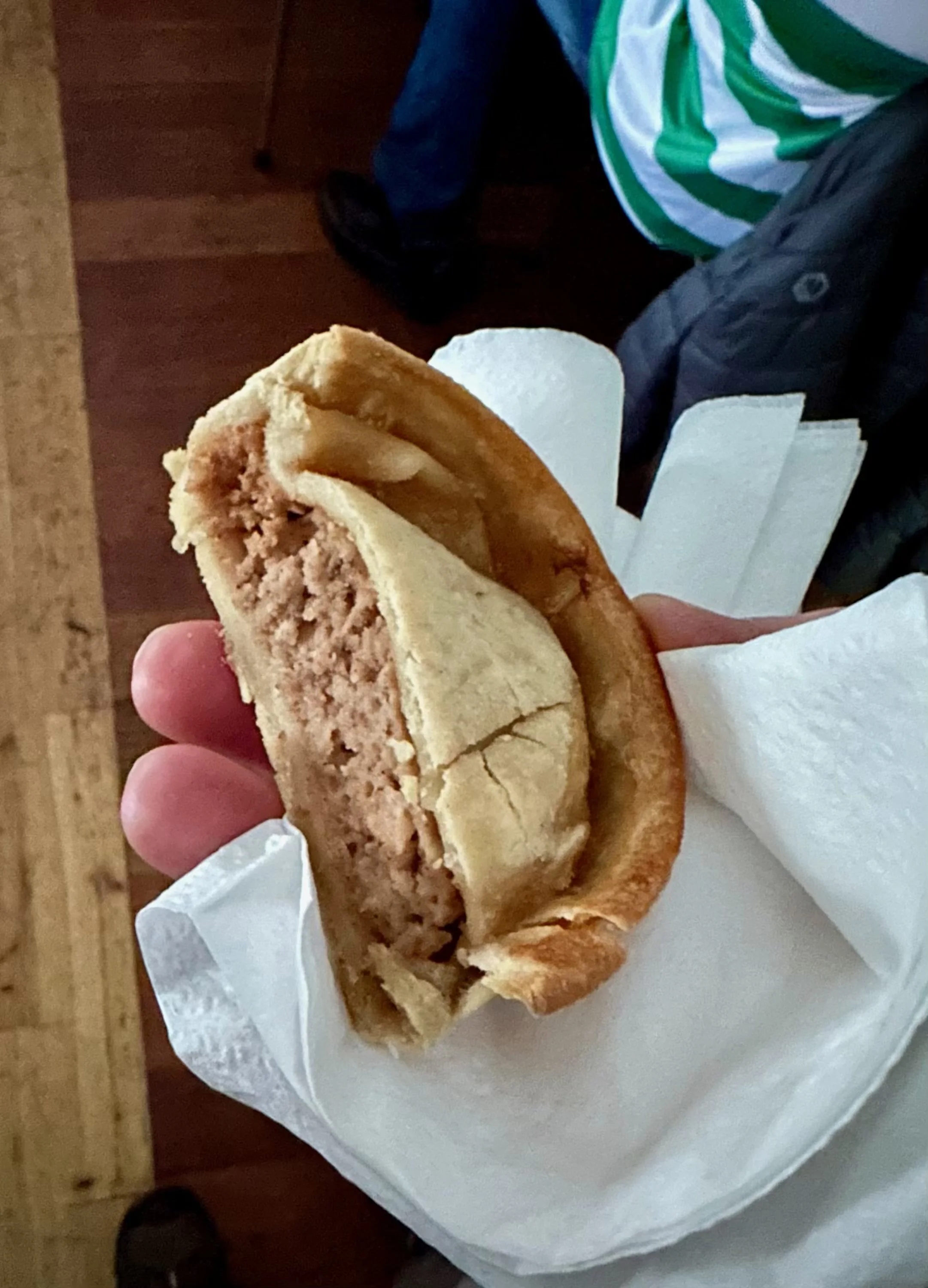 A hand holding a half-eaten, cooked sausage baked inside a bread roll, with some white napkins or paper wrapped around it.