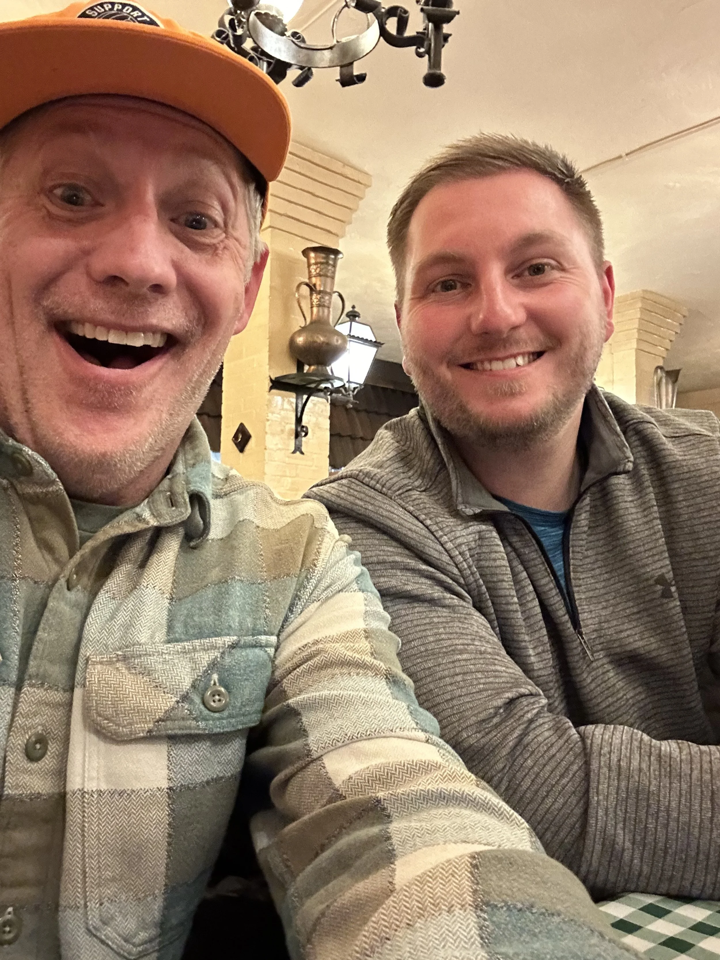 Two men smiling for a selfie in a restaurant or cafe setting