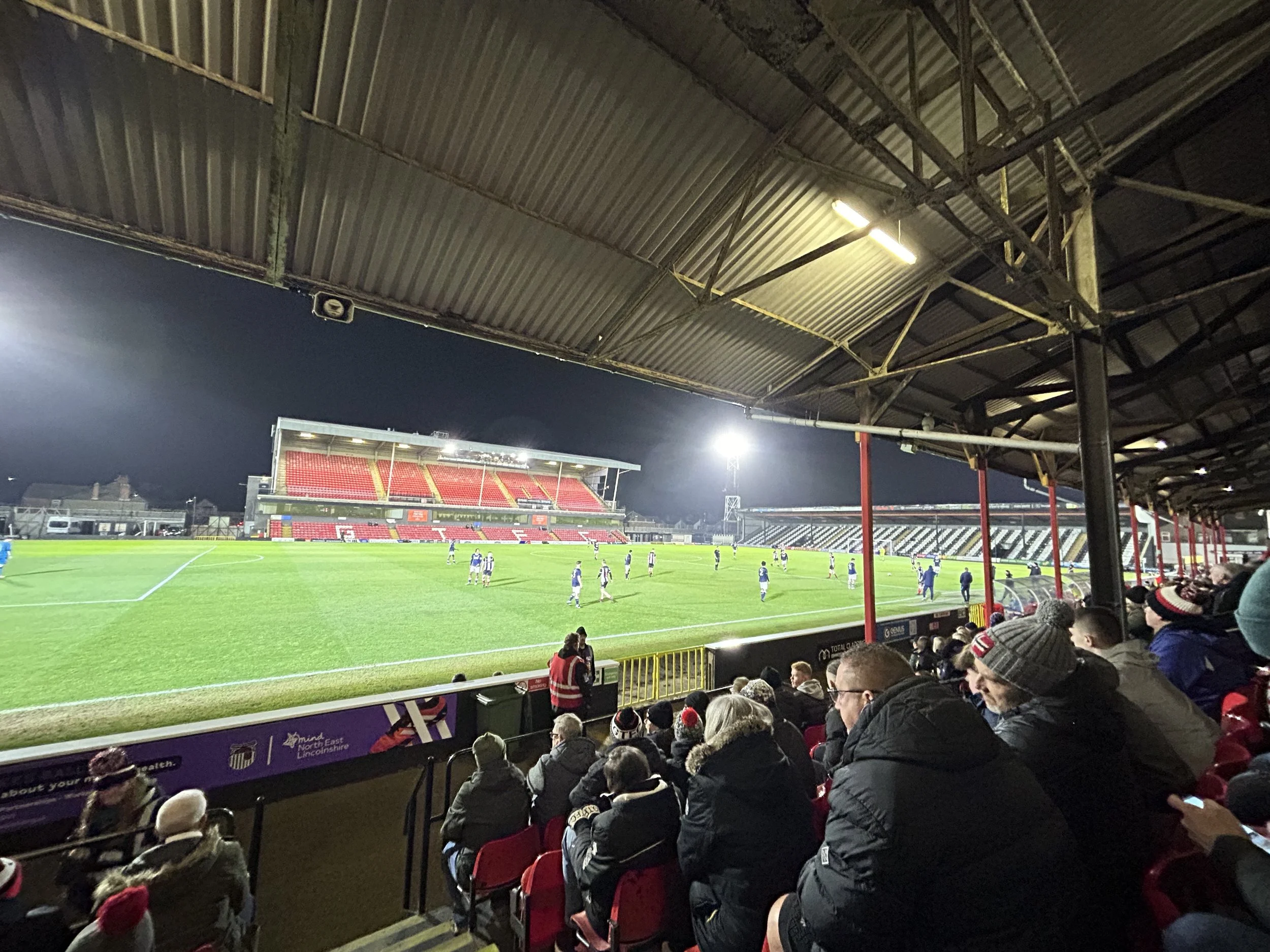 View of a football stadium at night with spectators seated in the stands and players on the field under bright lights.