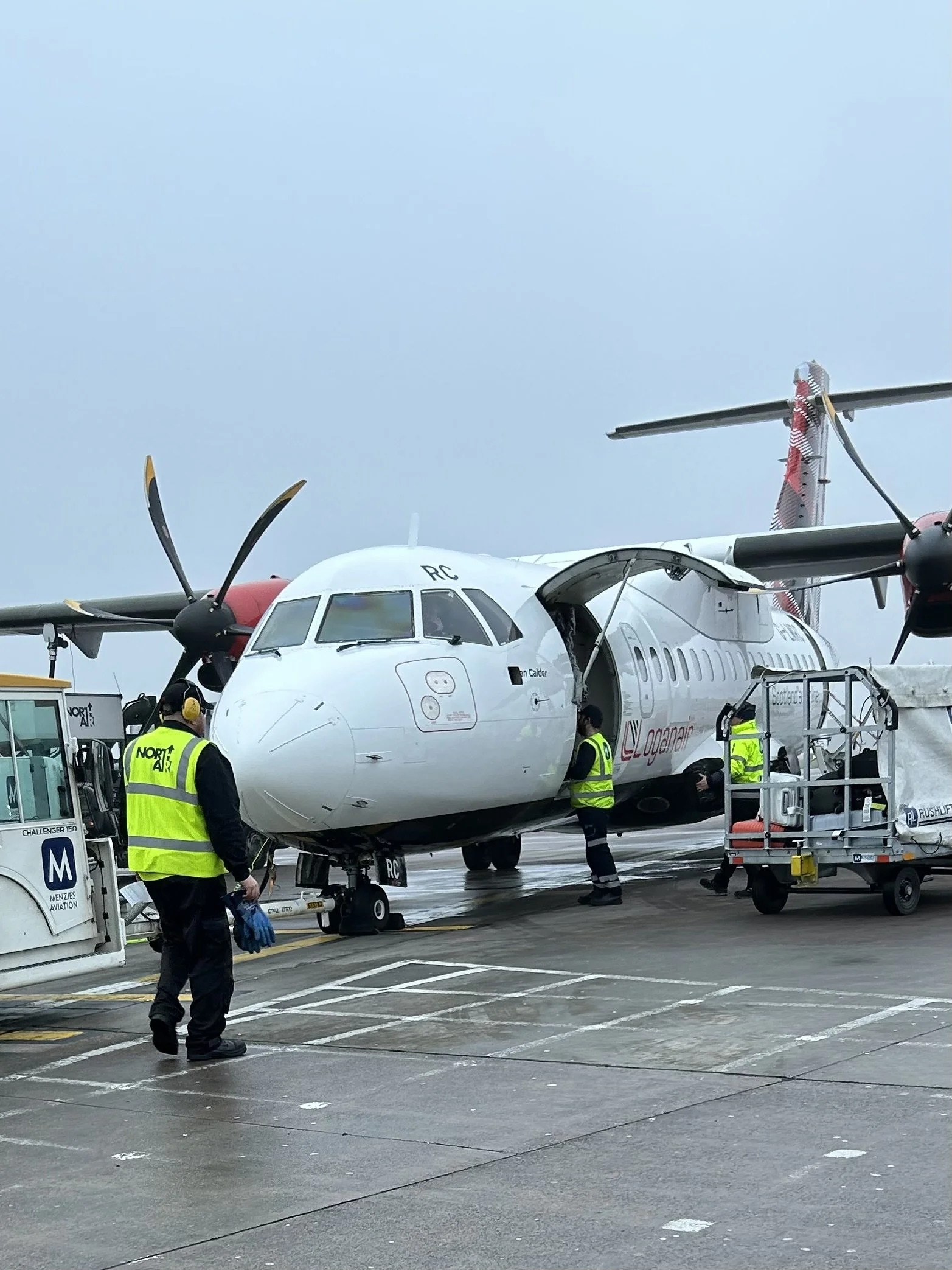 An airplane on the tarmac being serviced by ground crew in high-visibility vests under a cloudy sky.