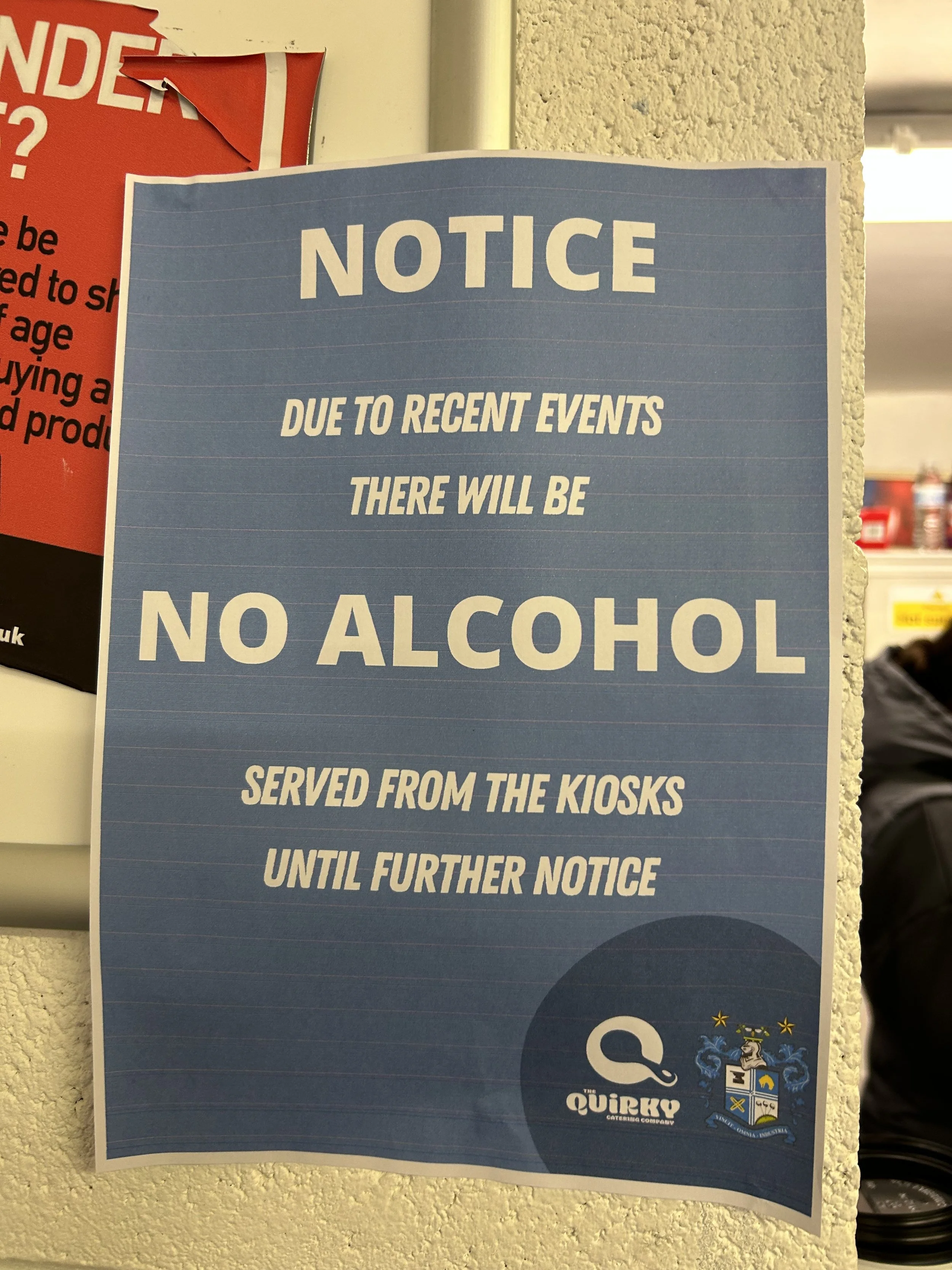 Blue notice sign with white text stating that due to recent events, there will be no alcohol served from the kiosks until further notice.