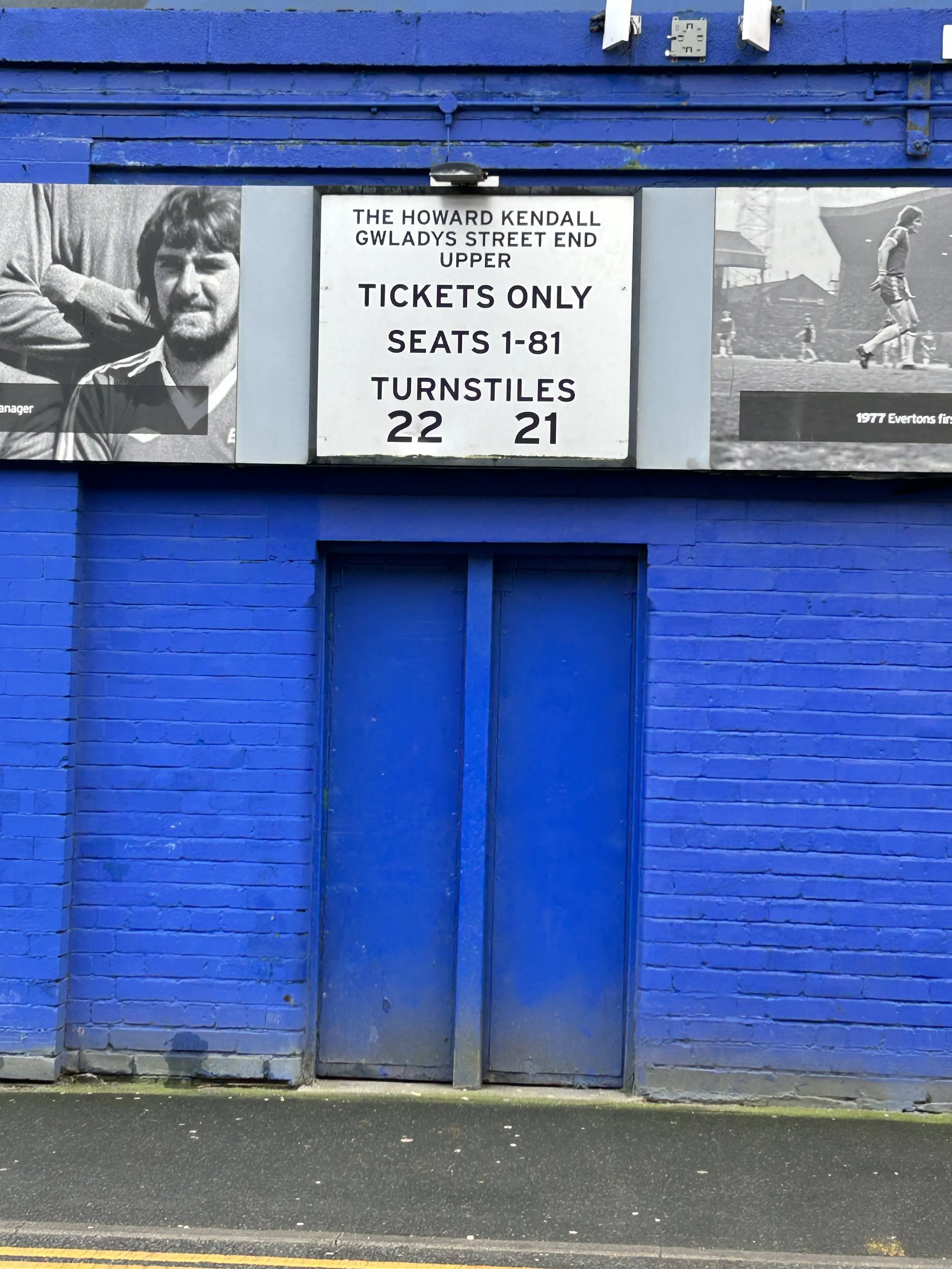Blue brick building with a large white sign indicating ticket and seating information for a sports venue, accompanied by black and white photographs of athletes.
