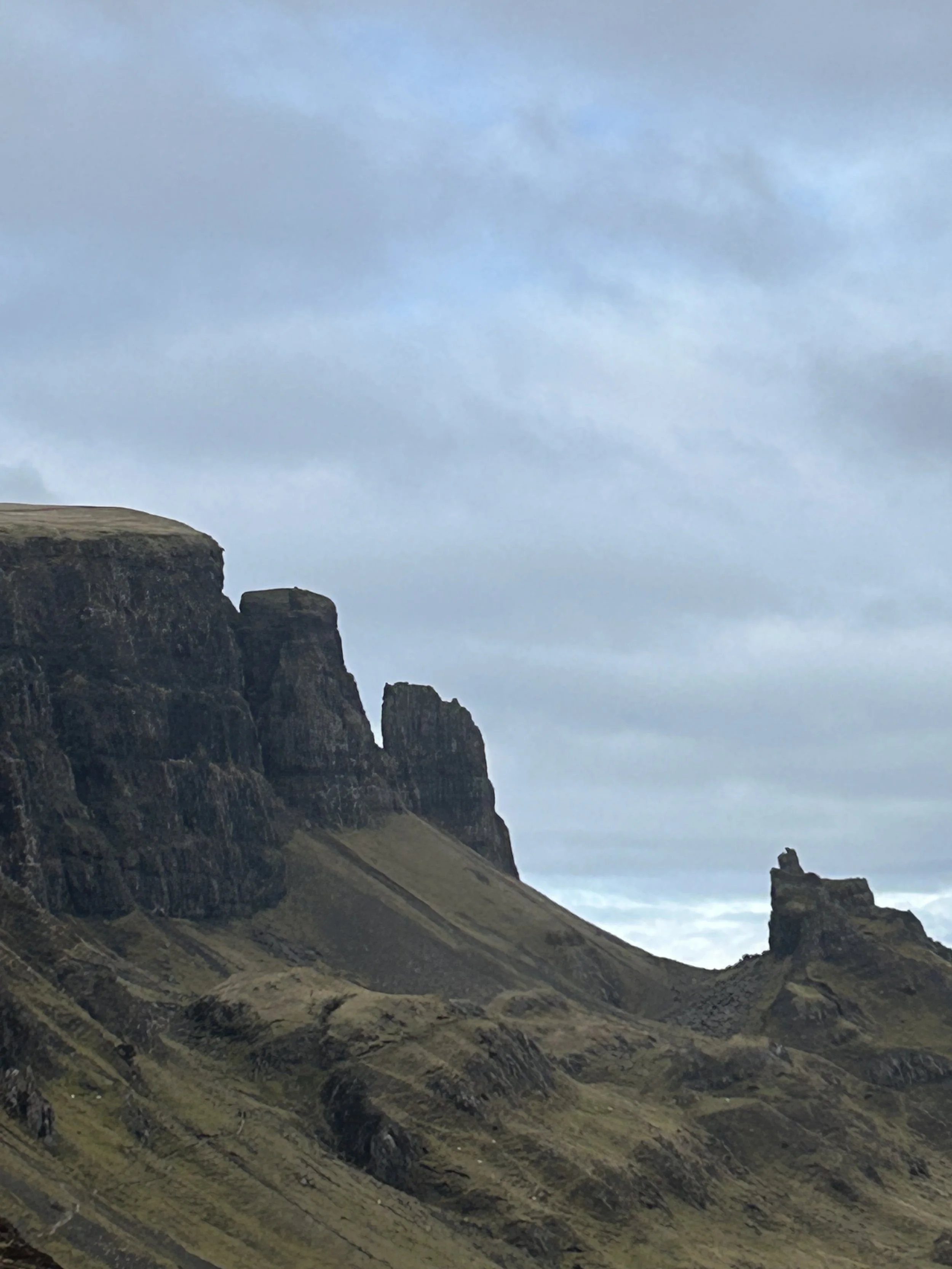 Scenic view of rugged mountains with steep cliffs and grassy slopes, under a cloudy sky.